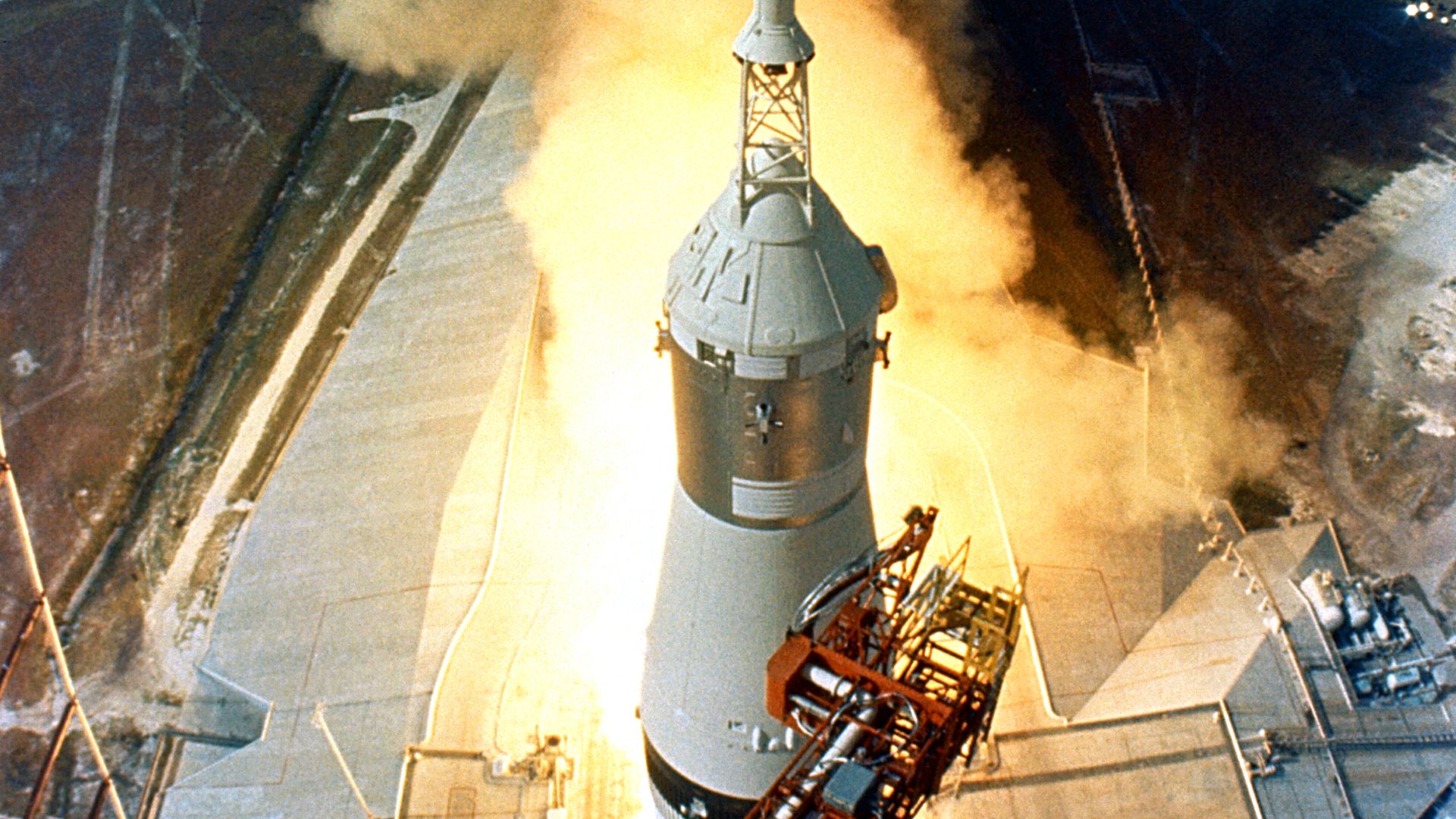 At 9:32 a.m. EDT, the swing arms move away and a plume of flame signals the liftoff of the Apollo 11 Saturn V space vehicle and astronauts Neil A. Armstrong, Michael Collins and Edwin E. Aldrin, Jr. from Kennedy Space Center Launch Complex 39A.