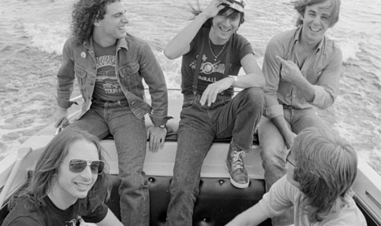 Steve Smith, Neal Schon, Steve Perry, Jonathan Cain, and Ross Valory (l to r) of the rock band Journey ride in a boat.