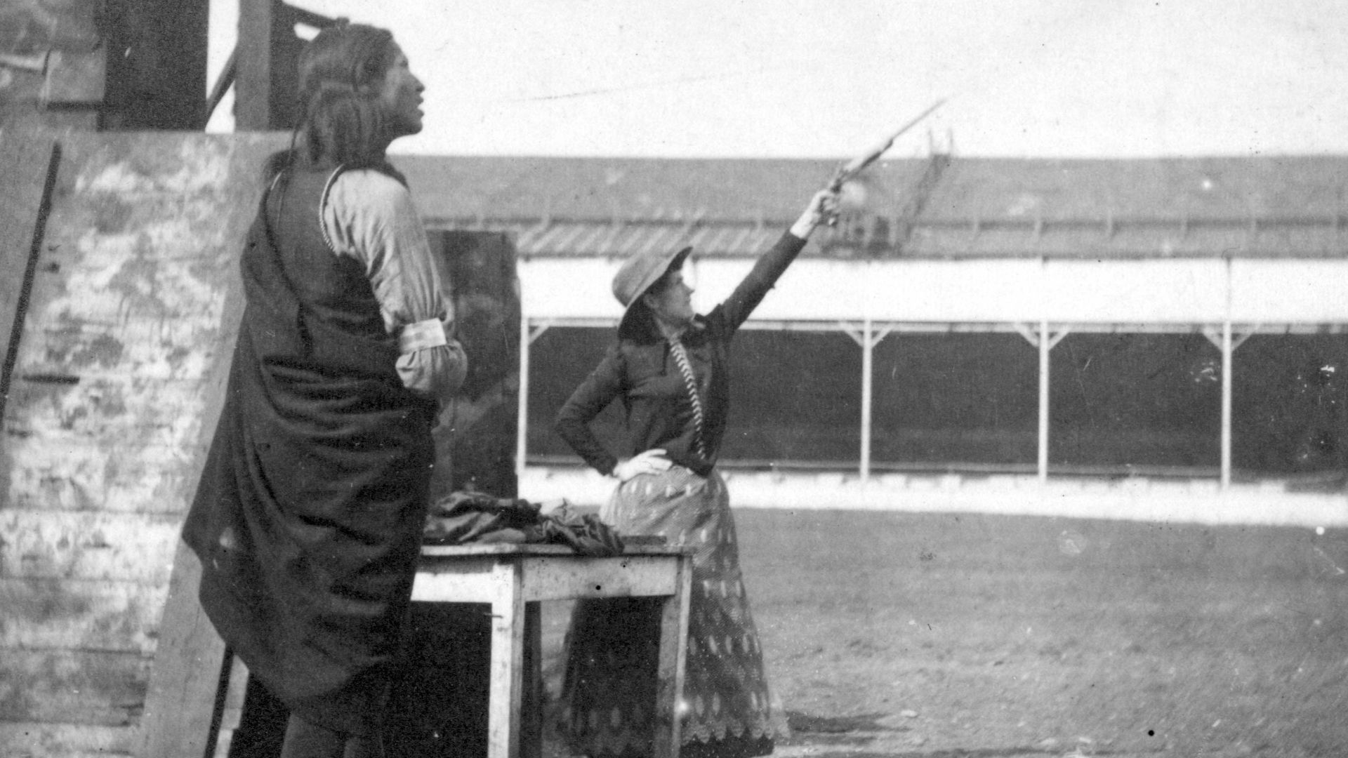 A Native American man stands in the left foreground watching Phoebe Anne