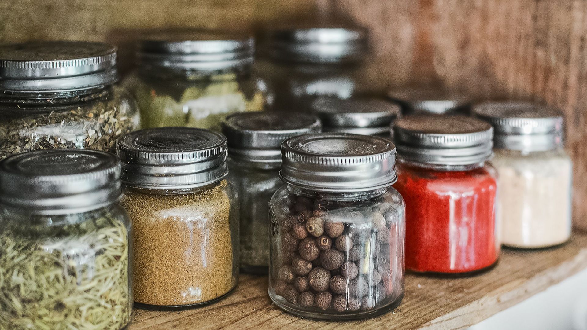 Close-up of assorted spice jars with various herbs on a kitchen shelf, showcasing colorful culinary ingredients.