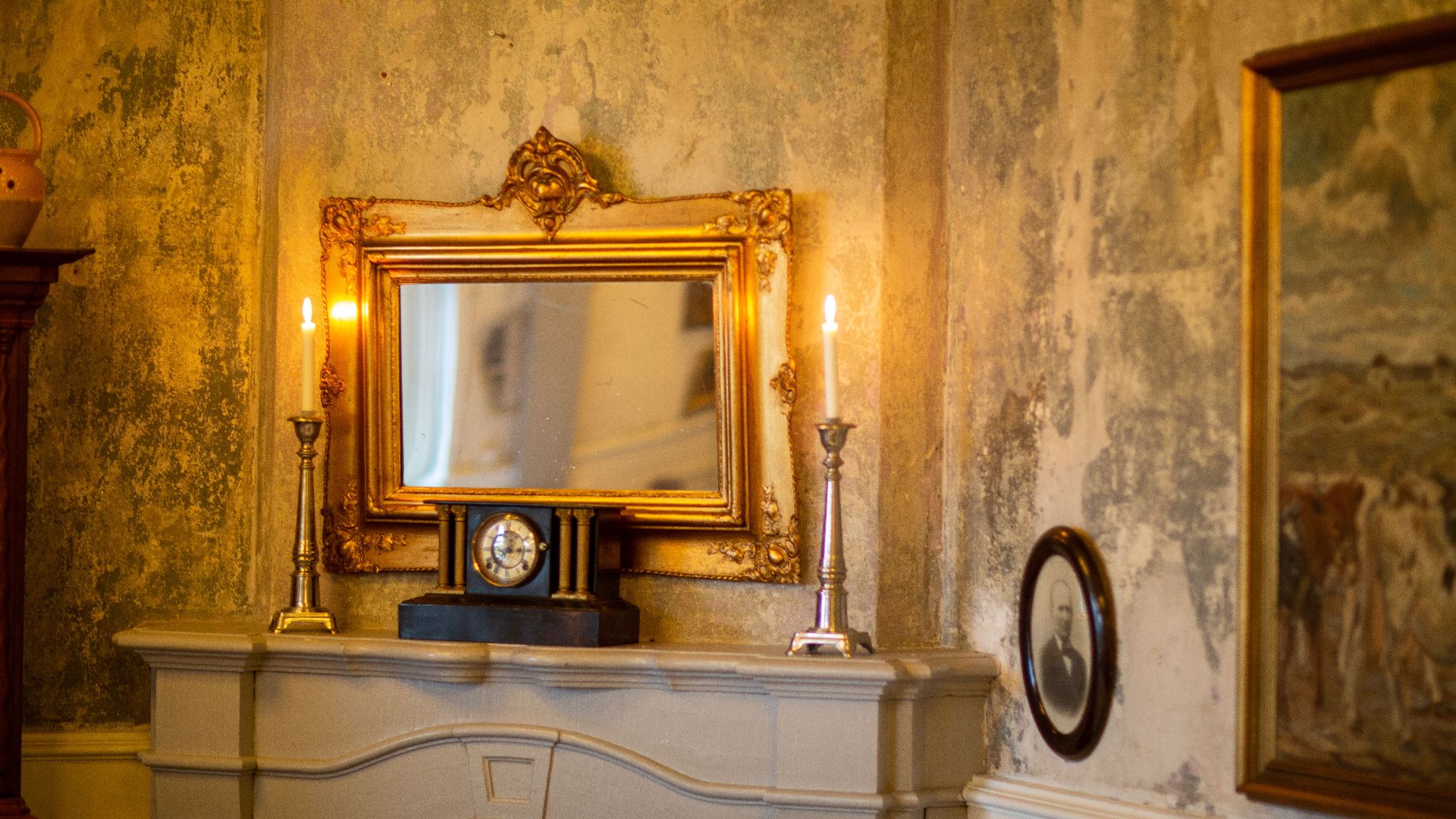 A classic interior scene featuring a golden mirror, lit candles, and antique decor on a mantel.