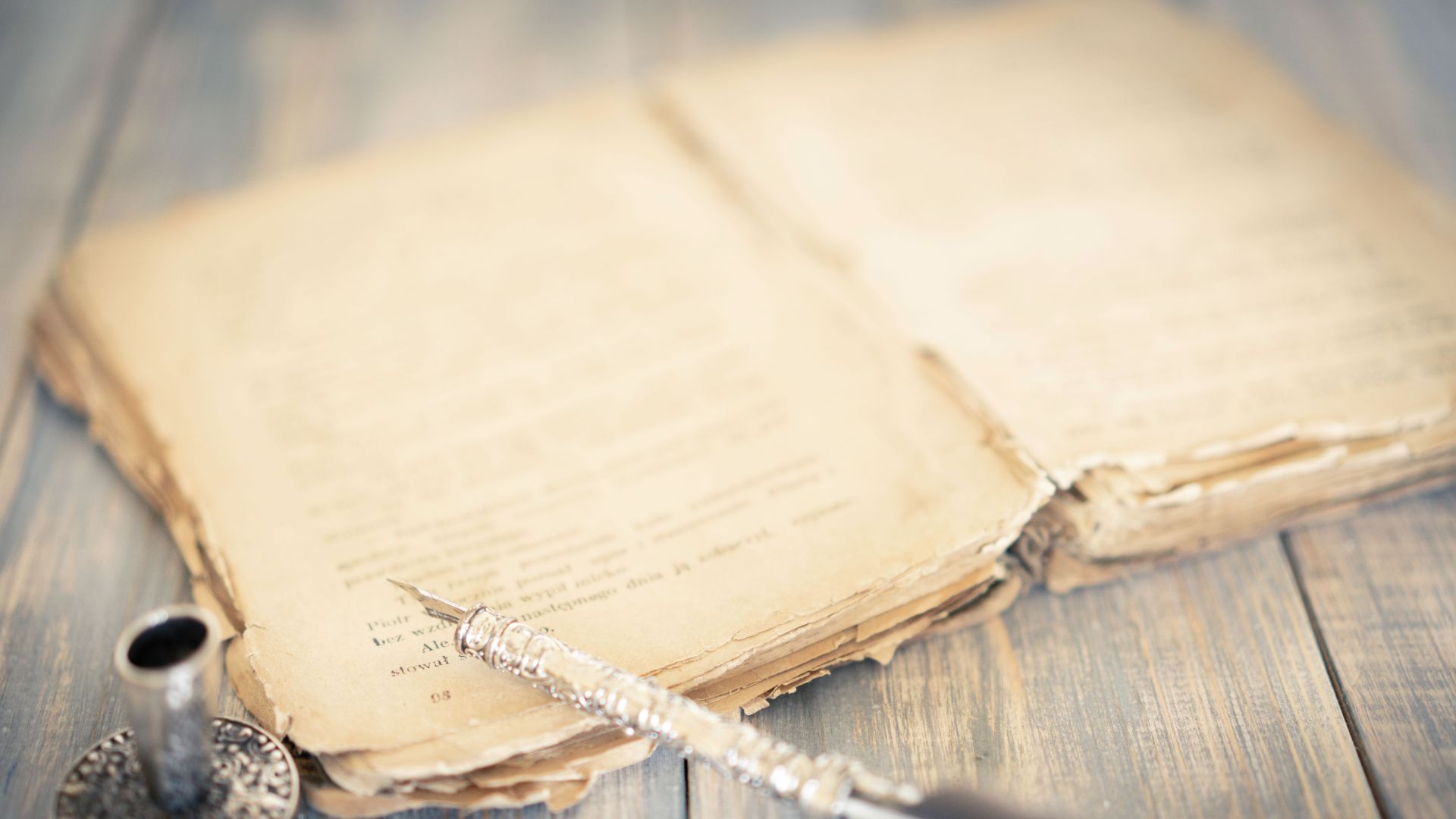 Close-up of an antique book and vintage pen on a rustic wooden table, evoking a sense of history and nostalgia.