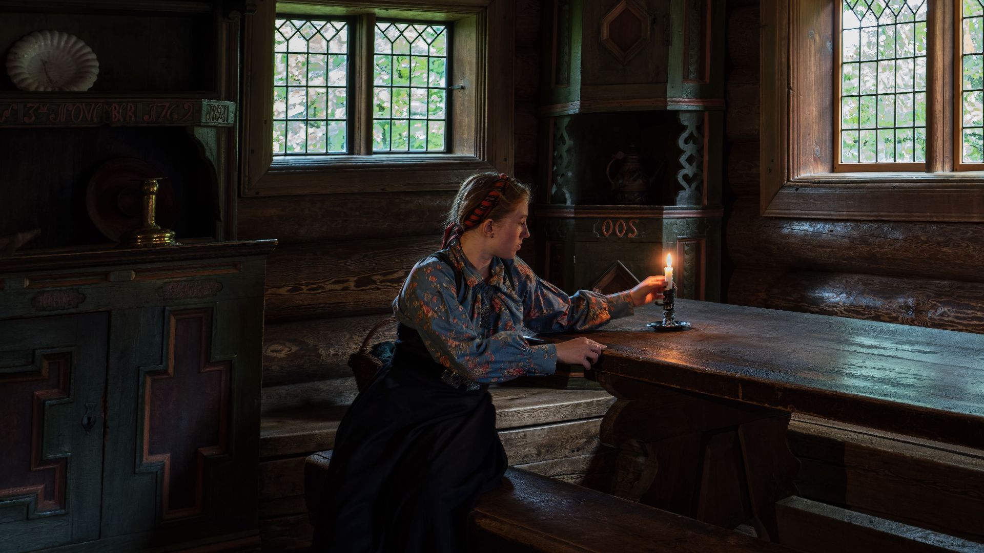 A woman sits by candlelight in a vintage wooden room, exuding a warm and nostalgic ambiance.