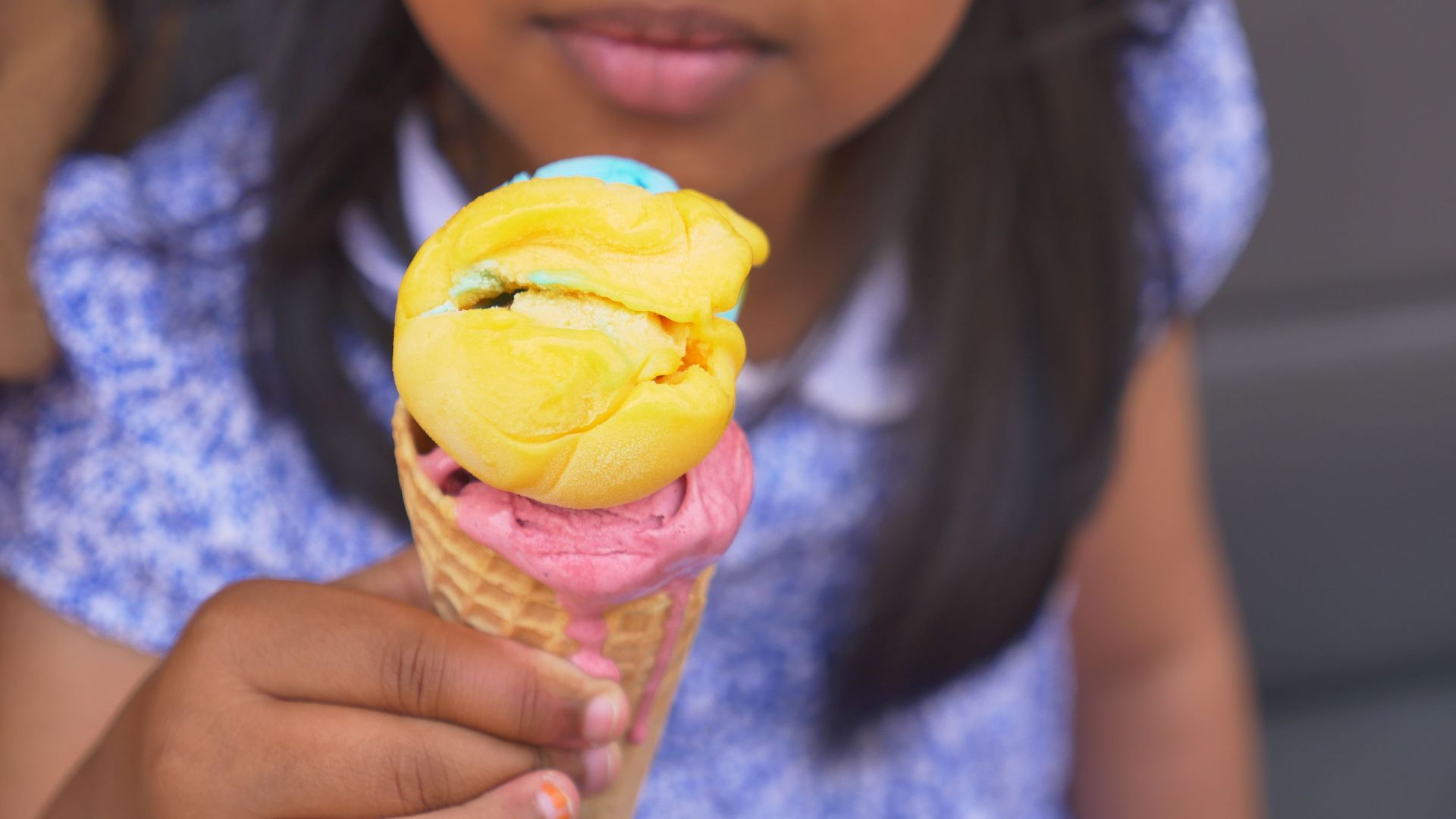 A child enjoys a vibrant multi-colored ice cream cone on a sunny day.