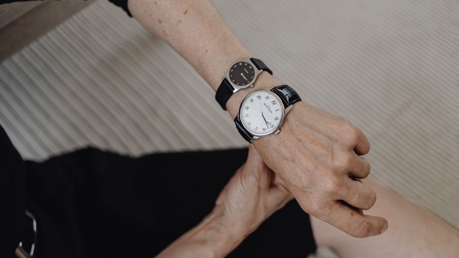 Elderly woman checking time on two wristwatches, symbolizing time management.