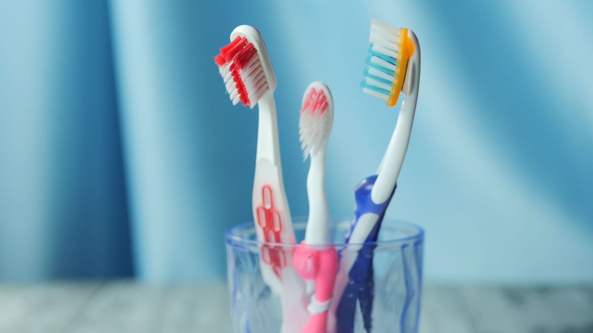 A trio of vibrant toothbrushes in a glass on a blue background, emphasizing dental hygiene.