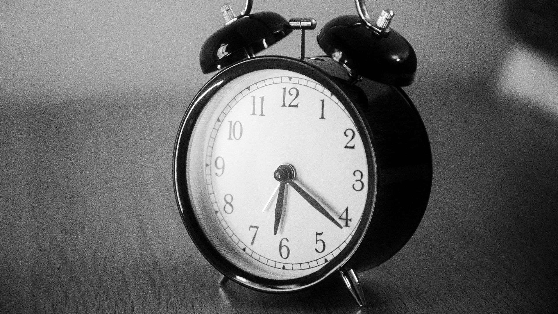 Close-up of a black vintage alarm clock showing precise time in grayscale.