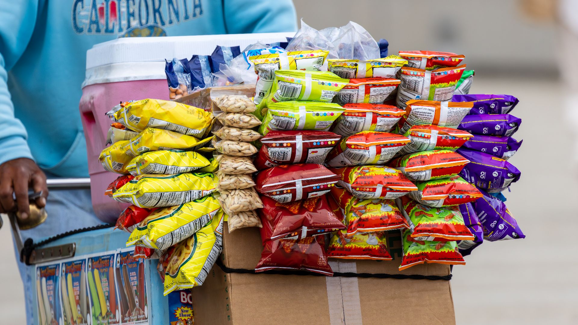 A street vendor's cart filled with a variety of colorful snack packets for sale outdoors.