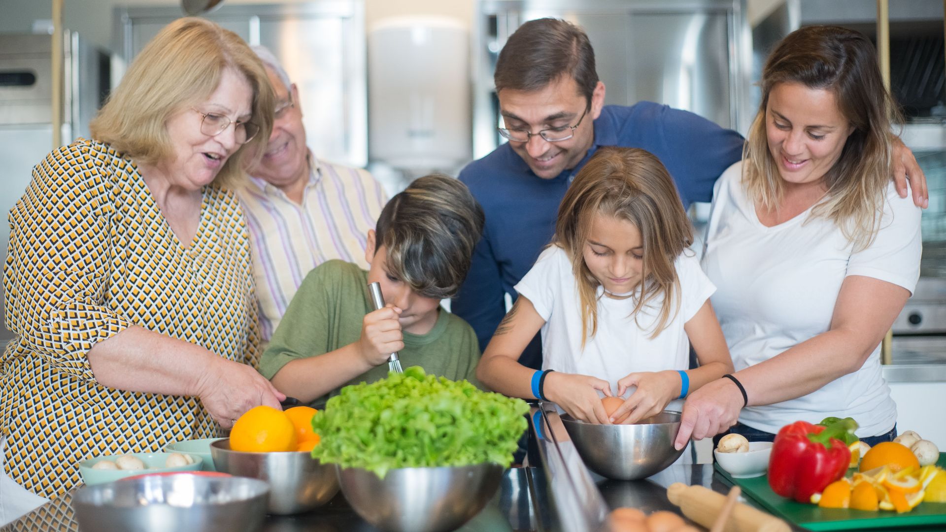 Family of various ages gathers in kitchen to cook meal together, showcasing culinary togetherness.