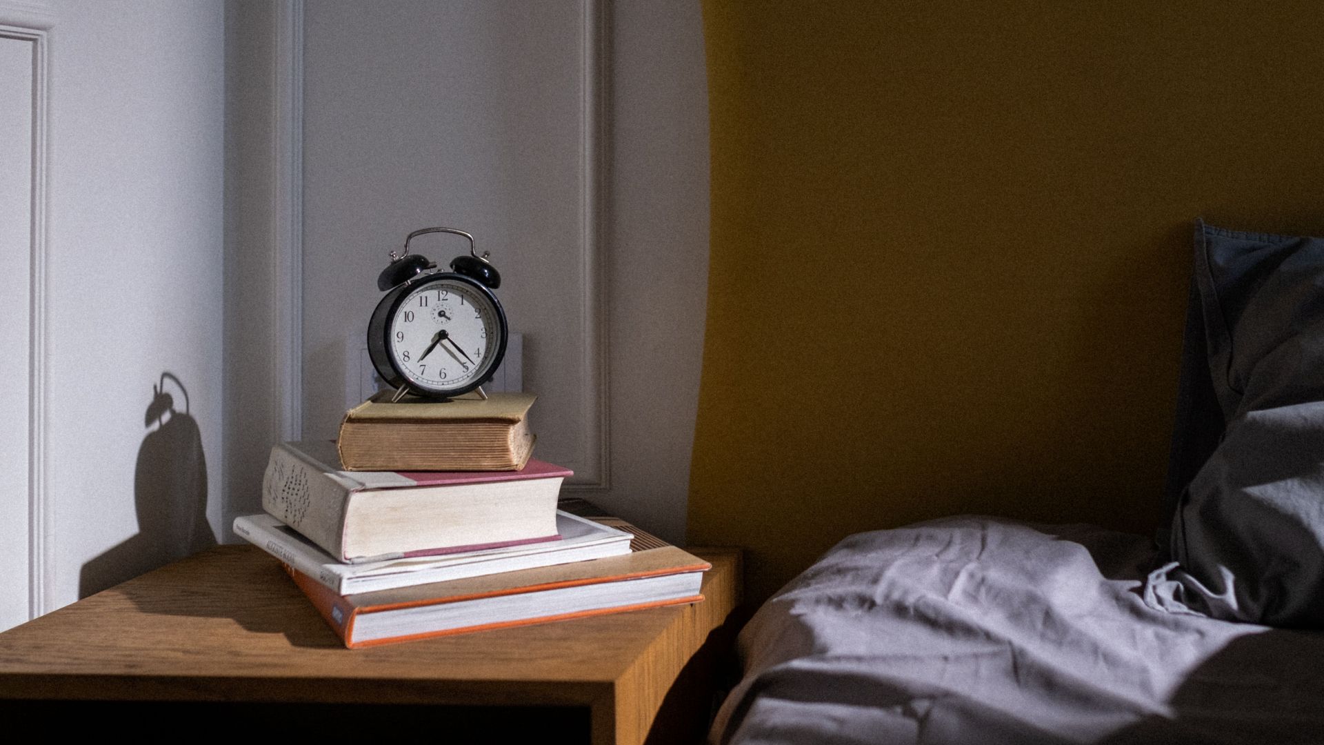 A cozy bedroom setting with books and an alarm clock on a nightstand next to a bed.