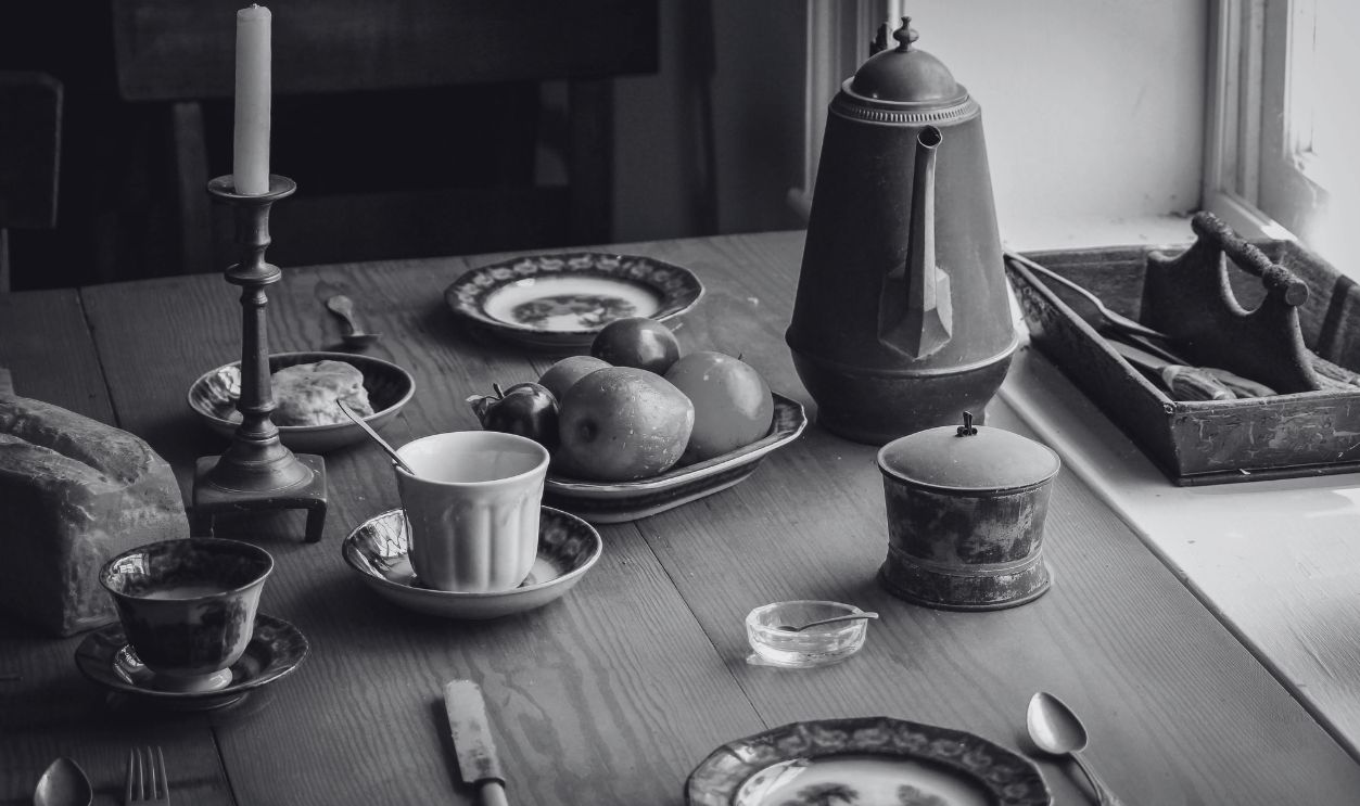 A rustic kitchen table scene with fruits, vintage utensils, and ceramic dishes