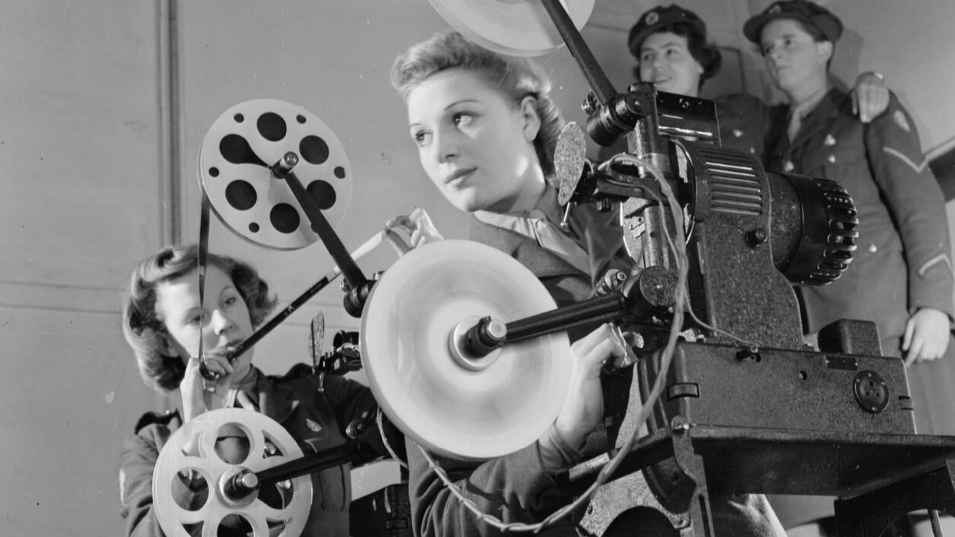 Ats Cine Projector Operators, Aldershot, Hampshire, England, UK, 1941
Two cine projectionists of the Auxiliary Territorial Service operate a 16mm De Vry Simplex Ampro projector at the field stores, Aldershot.  Behind them, two more ATS girls stand in the 