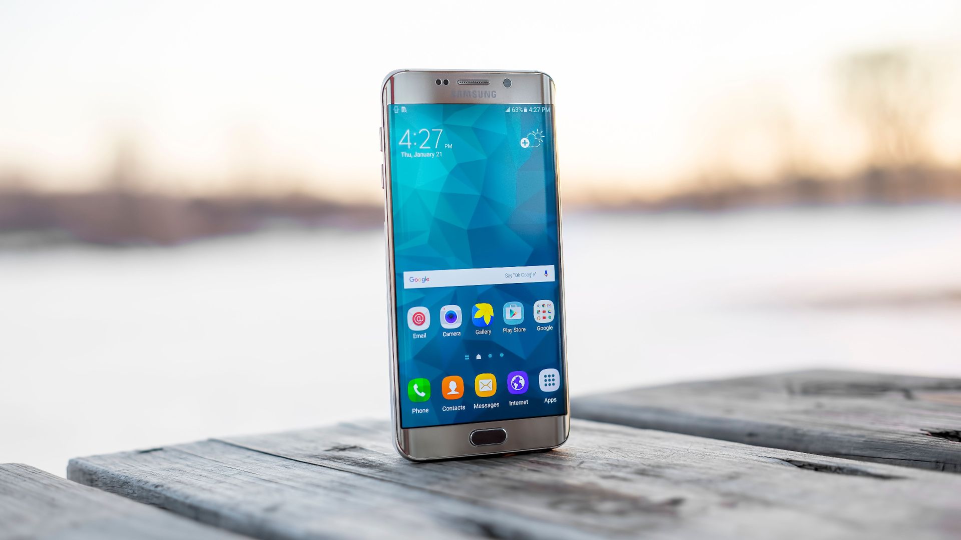 Samsung smartphone placed on a wooden surface outdoors during sunset.