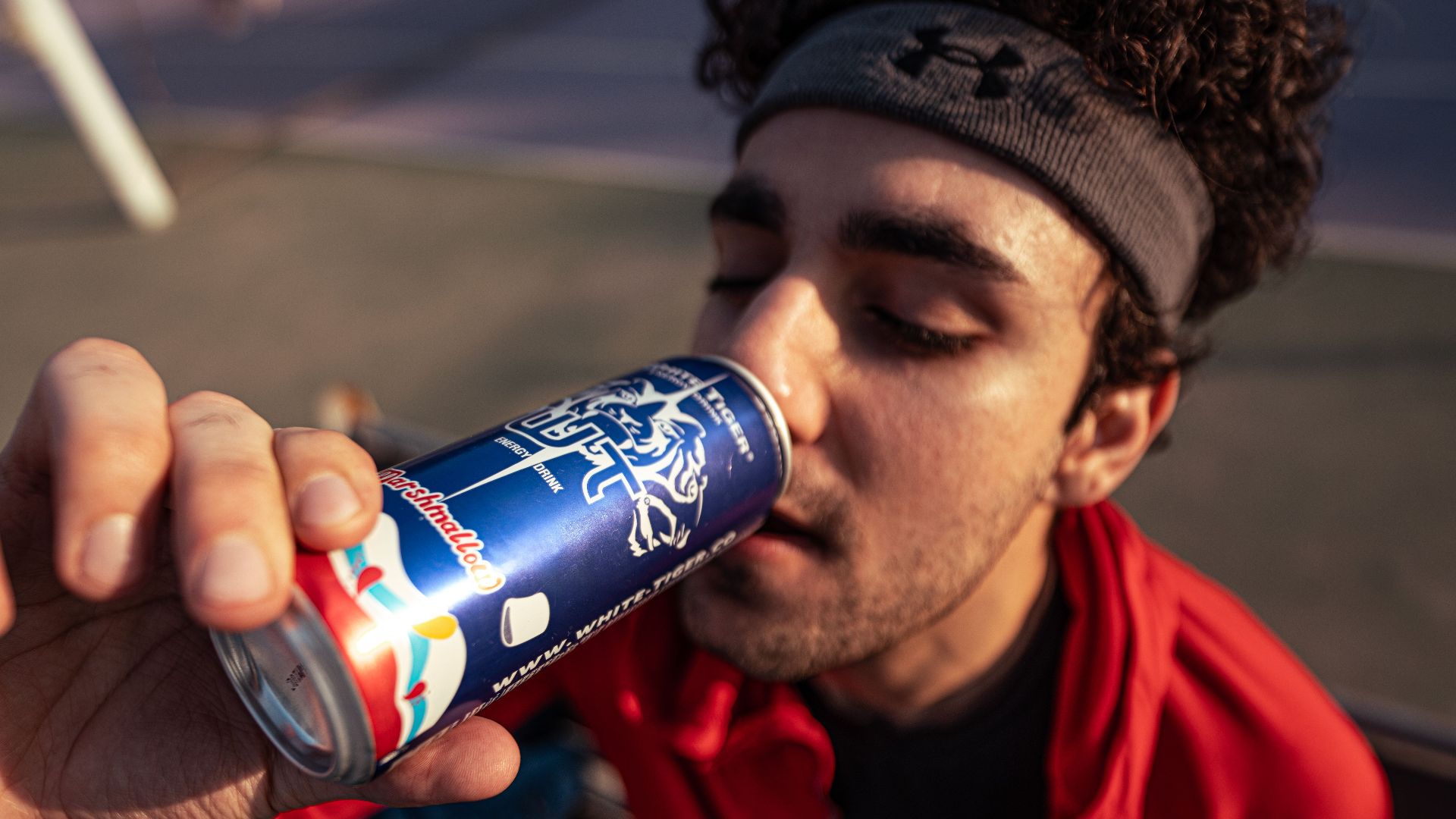 Young man enjoying a canned drink on a tennis court wearing sports clothing