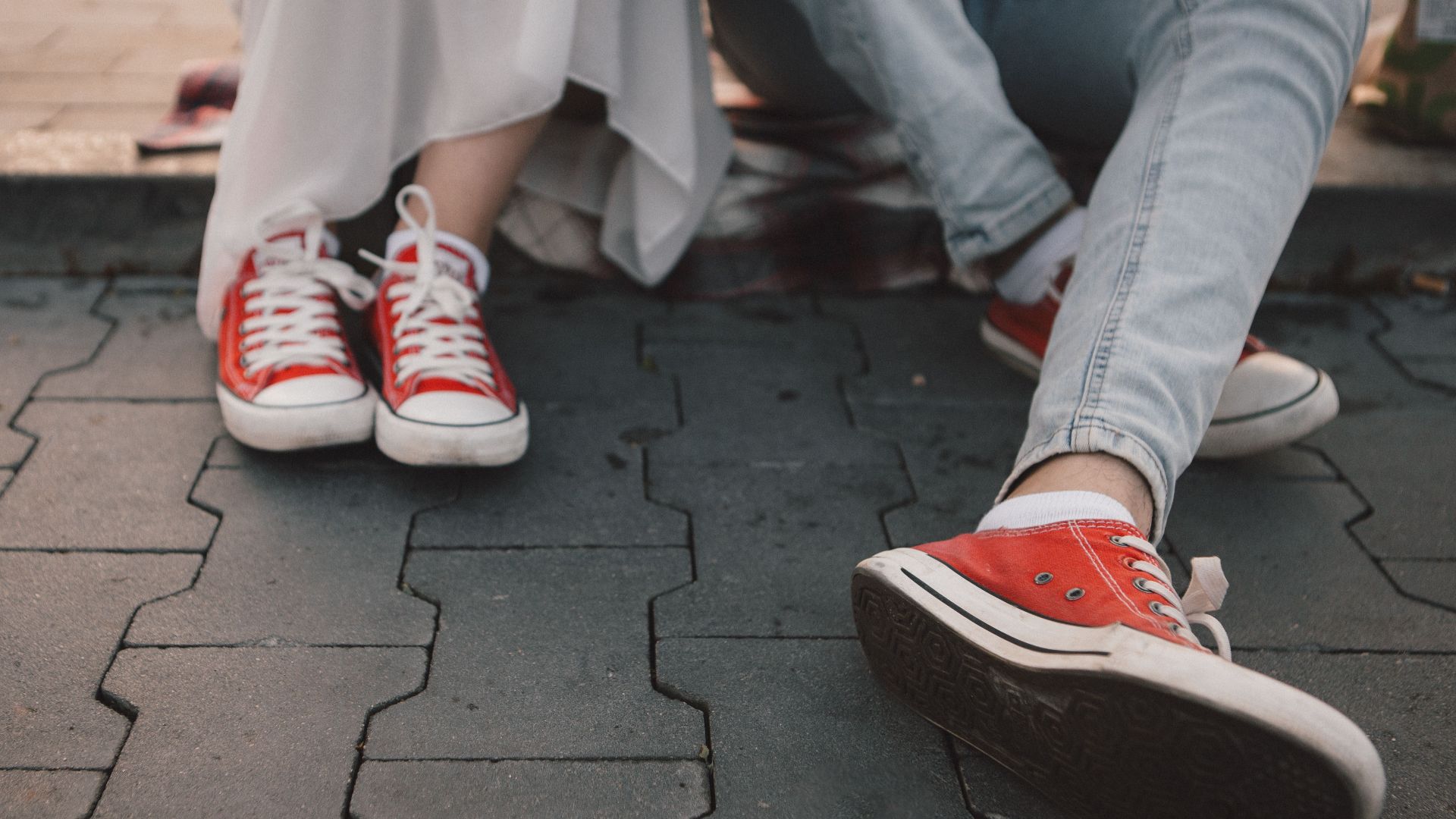 Two people wearing red sneakers sitting on urban pavement, showcasing casual and comfortable style.