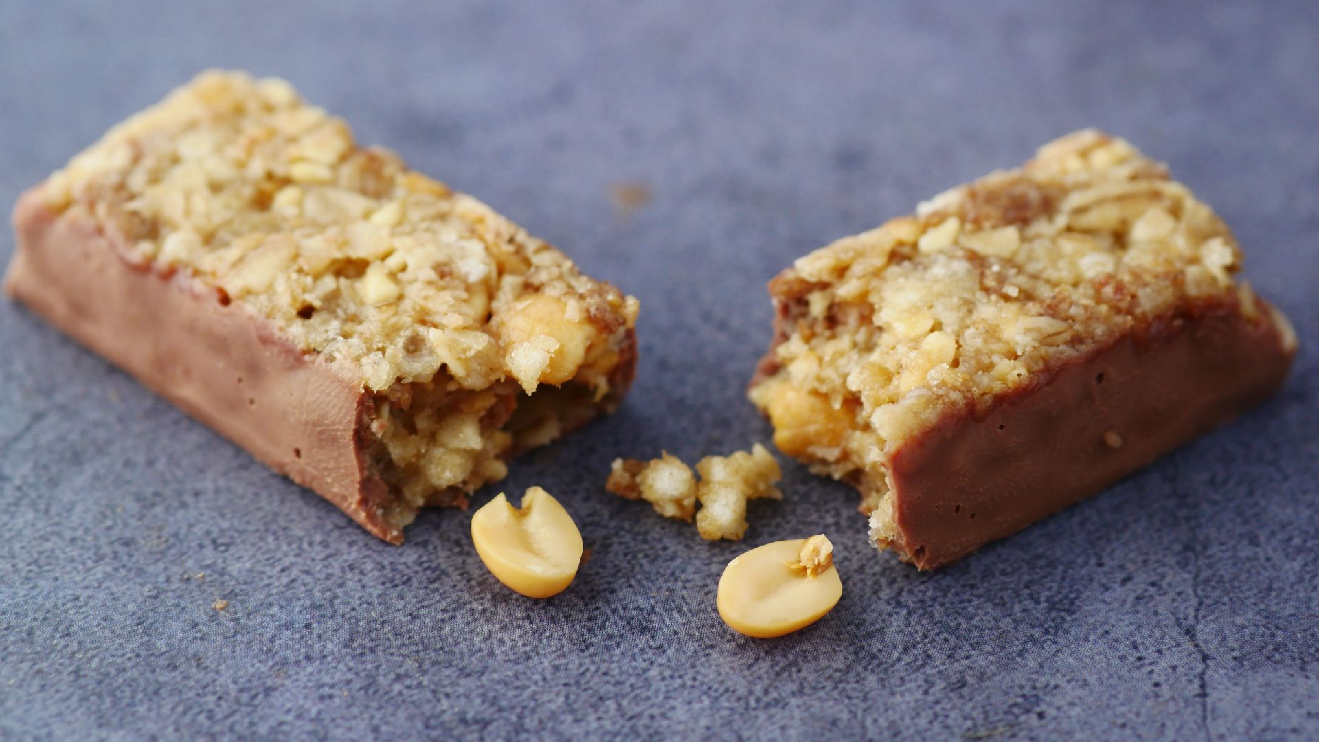 Close-up of a broken chocolate and nut energy bar on a gray surface.