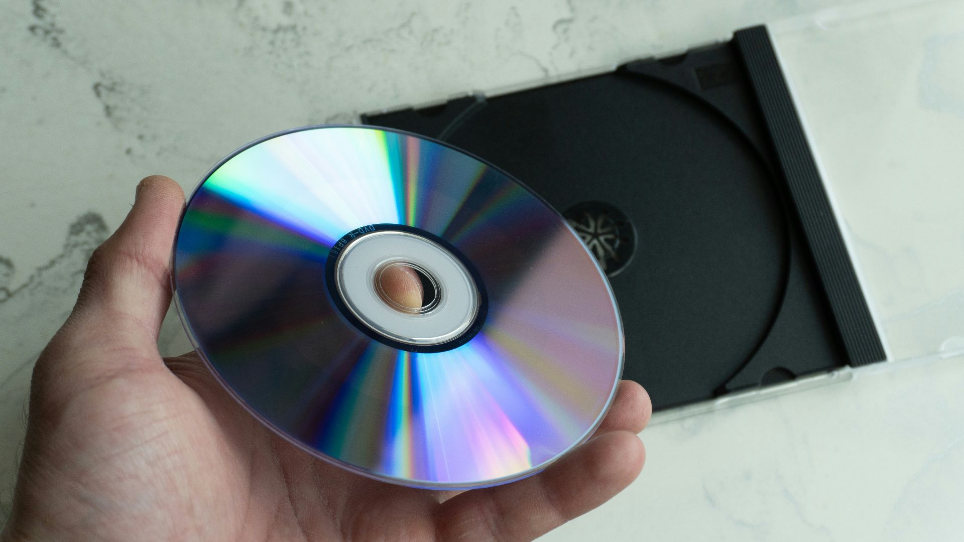 Hand holding a shiny cd with a case behind.