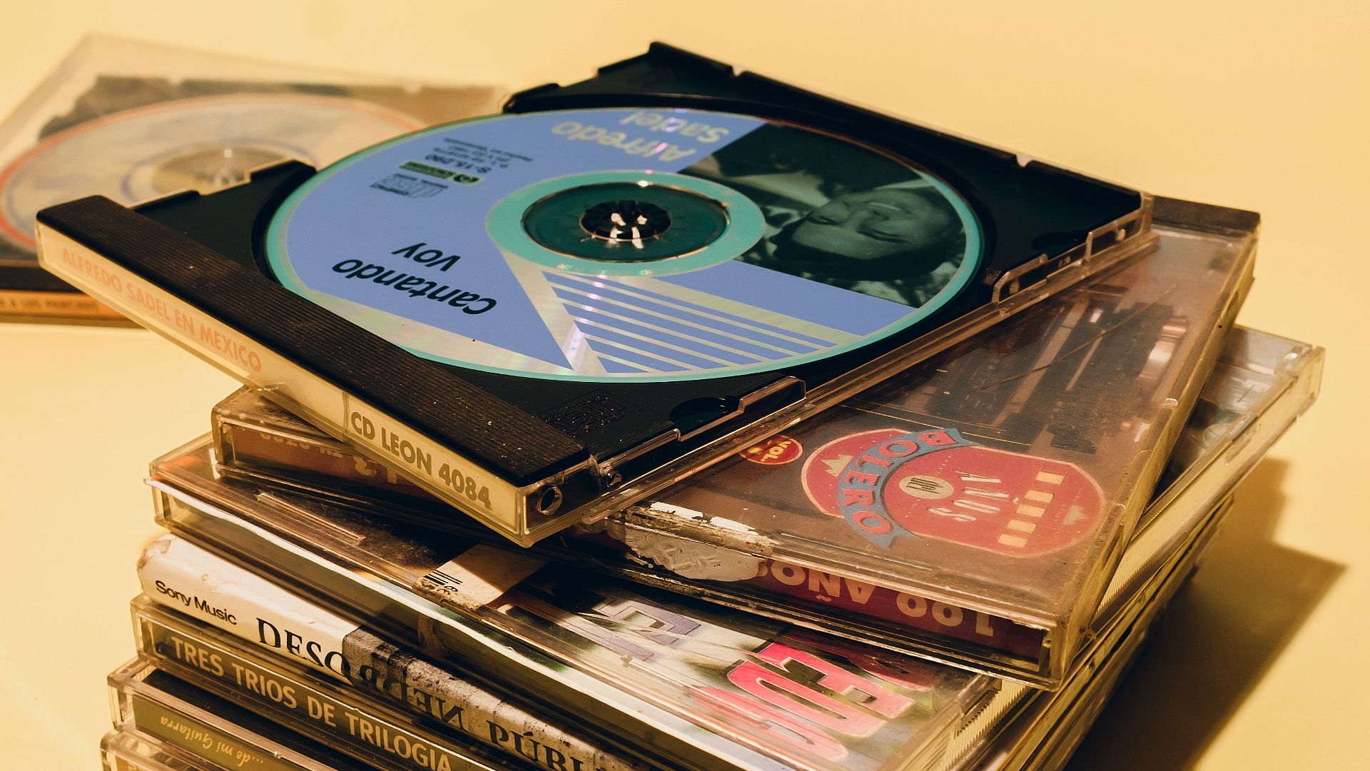 Vertical shot of a colorful stack of music CDs on a yellow surface, showcasing retro album art and jewel cases.