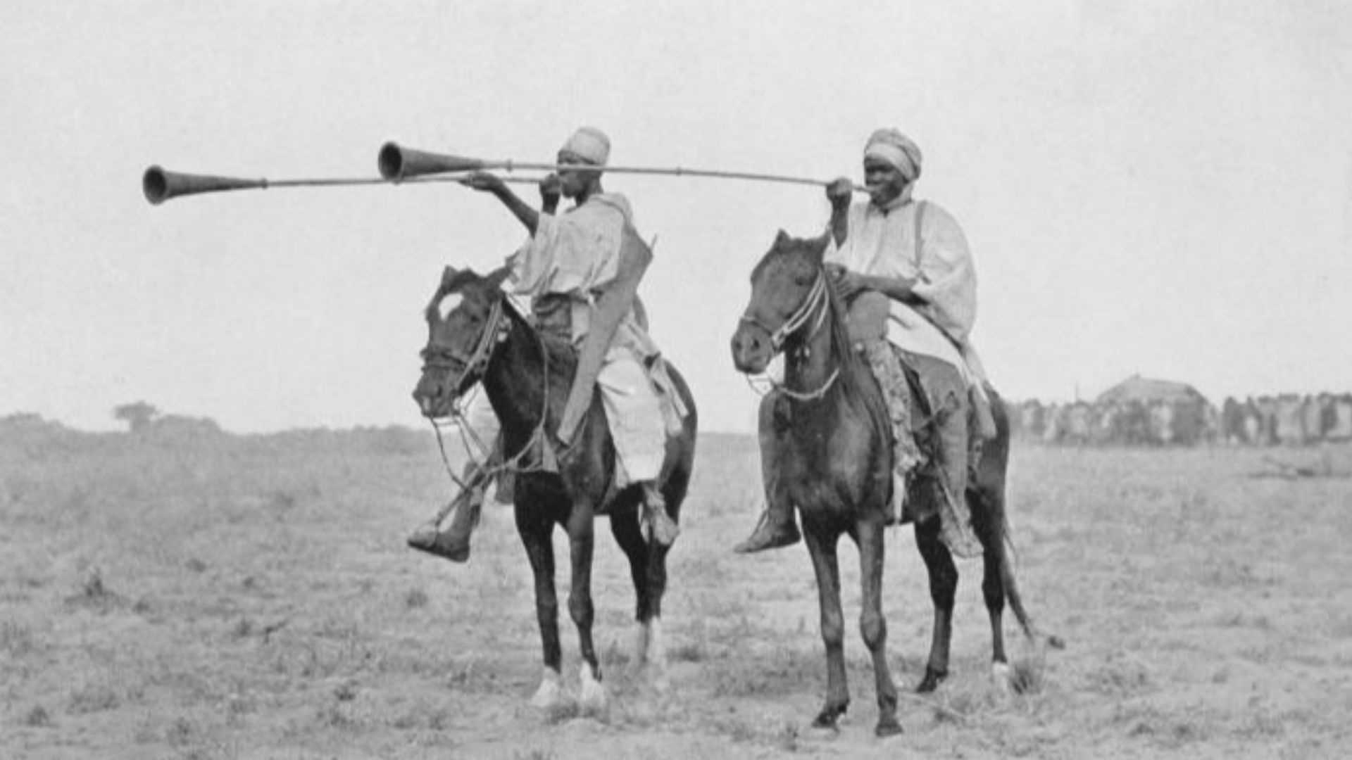 Two horse-mounted trumpeters in the Borno Emirate. Instrument not named,  but modern instuments of this kind are called kakaki.