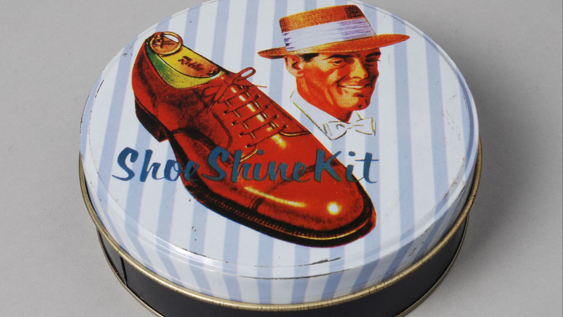 Objectgegevens Titel:  	Doos met schoenpoetsmiddelen “Shoe Shine Kit” Beschrijving:  	Doos (A) met deksel (B) met schoenpoetsartikelen. Op de deksel een hoofd van een man met hoed en een schoen en tekst op een gestreepte achtergrond. Herkomst:  	schoenenw