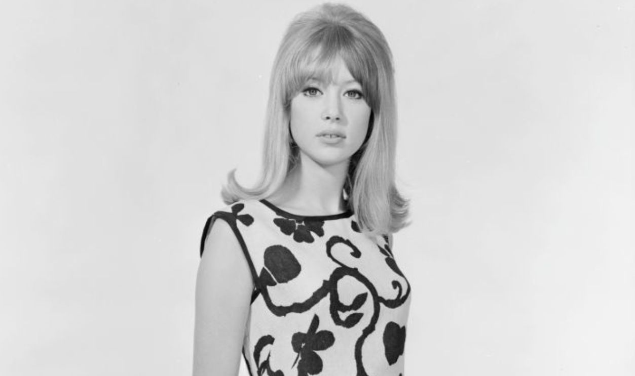1964: Patti Boyd models a Brilkie sleeveless sheath dress with a large, stylised floral pattern. She is holding the Beatles album 'A Hard Day's Night'. 