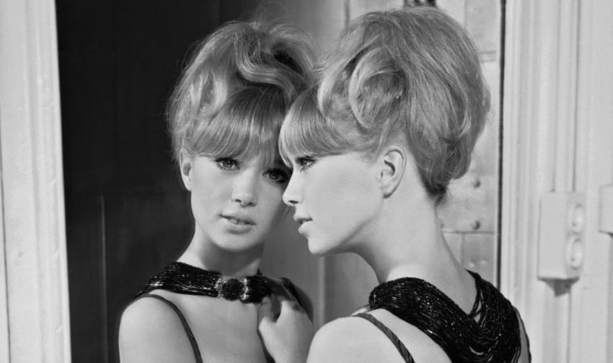 1964: Patti Boyd in a bare-shouldered evening dress and an elaborate bead necklace leans wistfully against a full-length mirror.