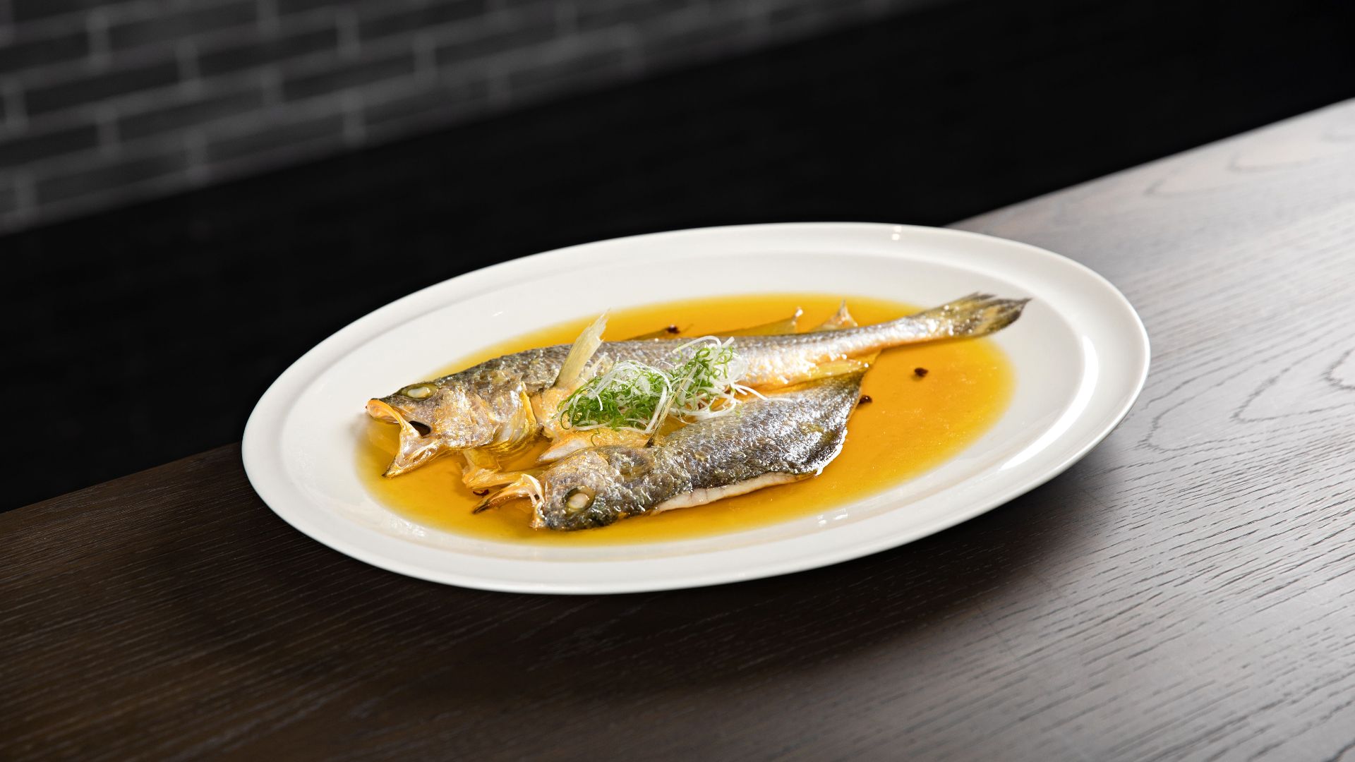 Two cooked fish on a plate with sauce and garnishes, ready to serve.
