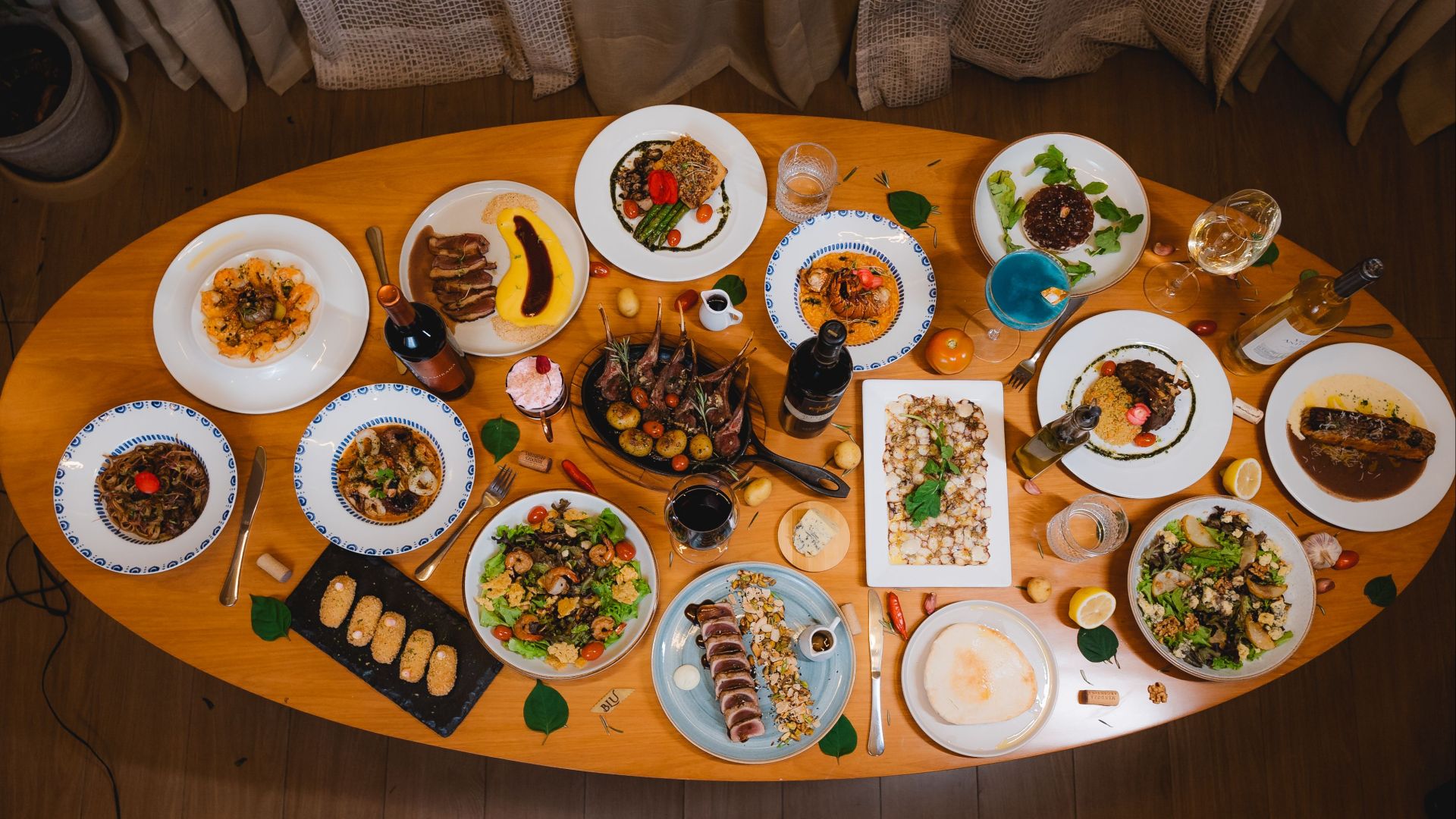 Top view of an elegant dining table set with diverse gourmet dishes and wine bottles.