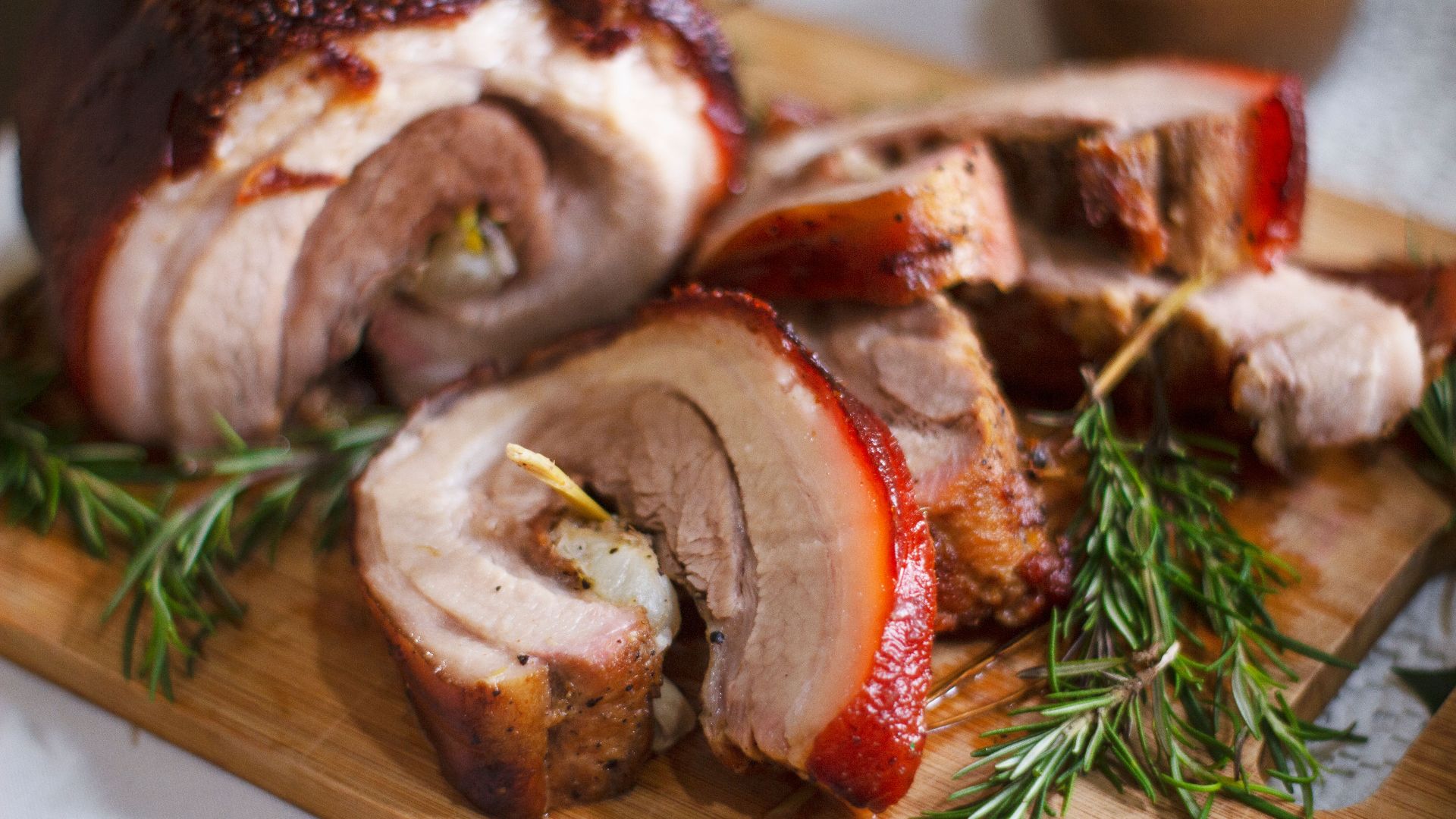 Delicious roasted porchetta slices on a wooden board with rosemary garnish, showcasing Italian cuisine.