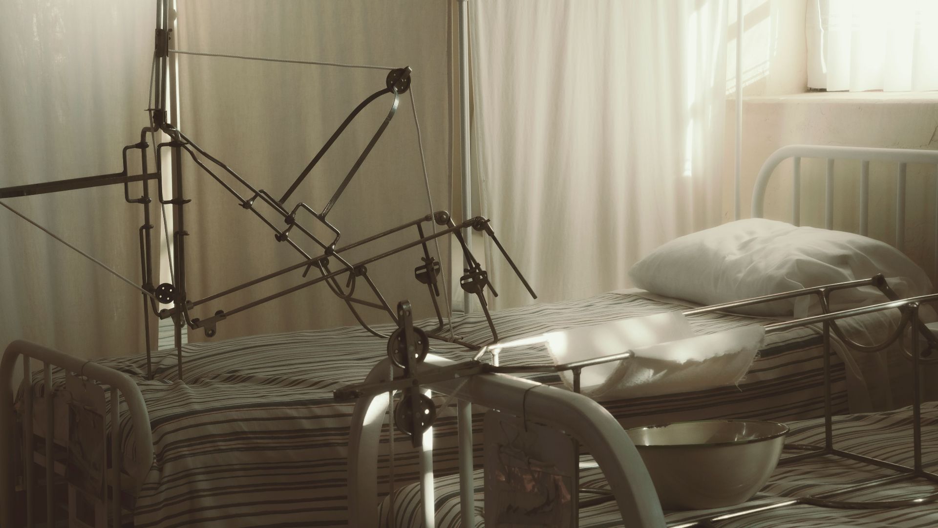 An empty hospital bed surrounded by medical equipment in a quiet, sunlit room.