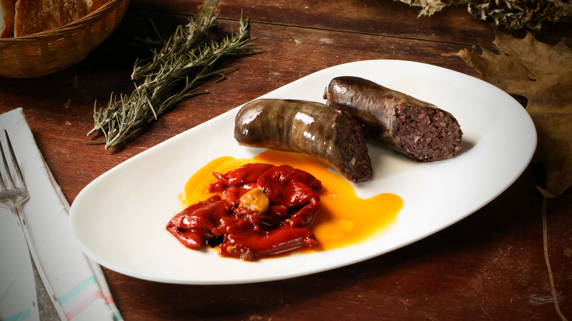 A rustic presentation of blood sausage with roasted red peppers and bread on a wooden table.