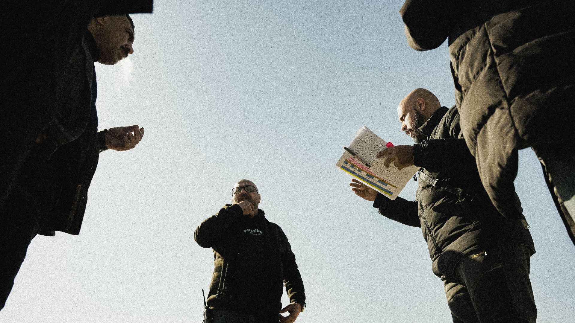 Group of men discussing something outdoors with notes and gestures.