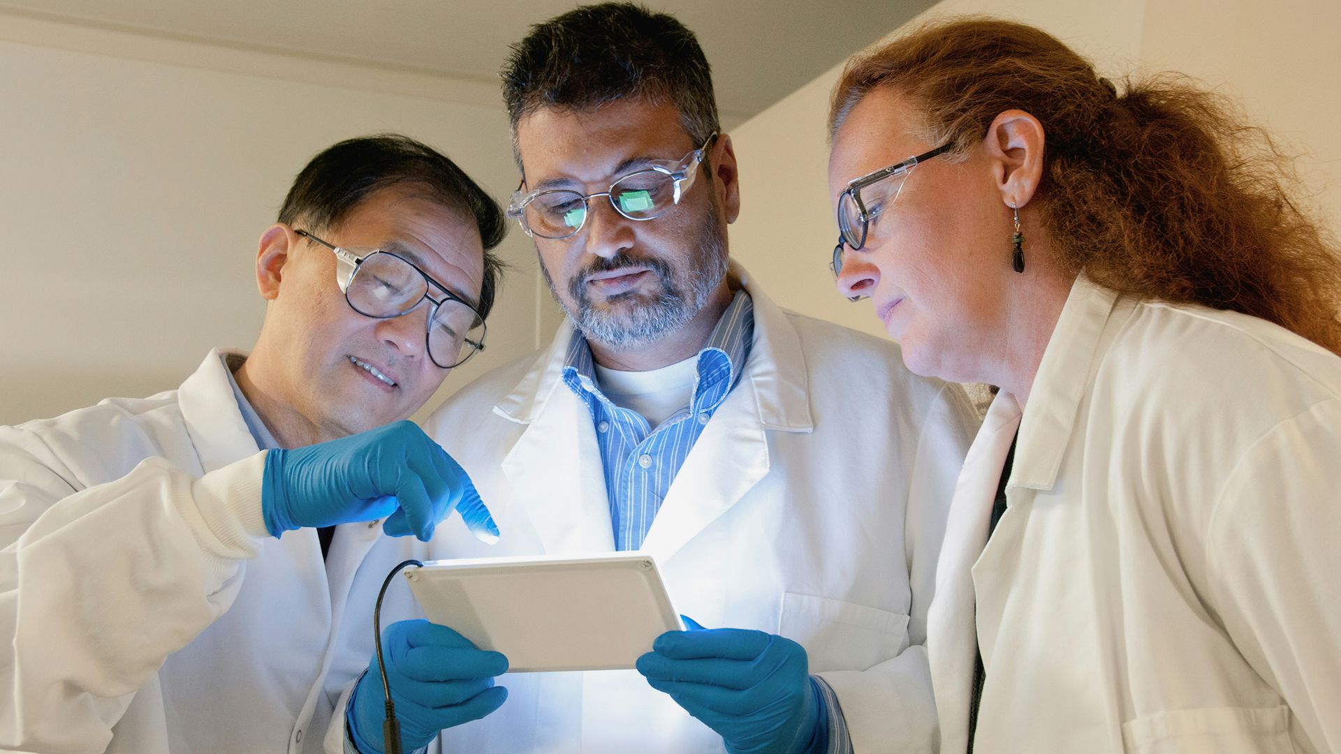 three people in lab coats looking at a tablet
