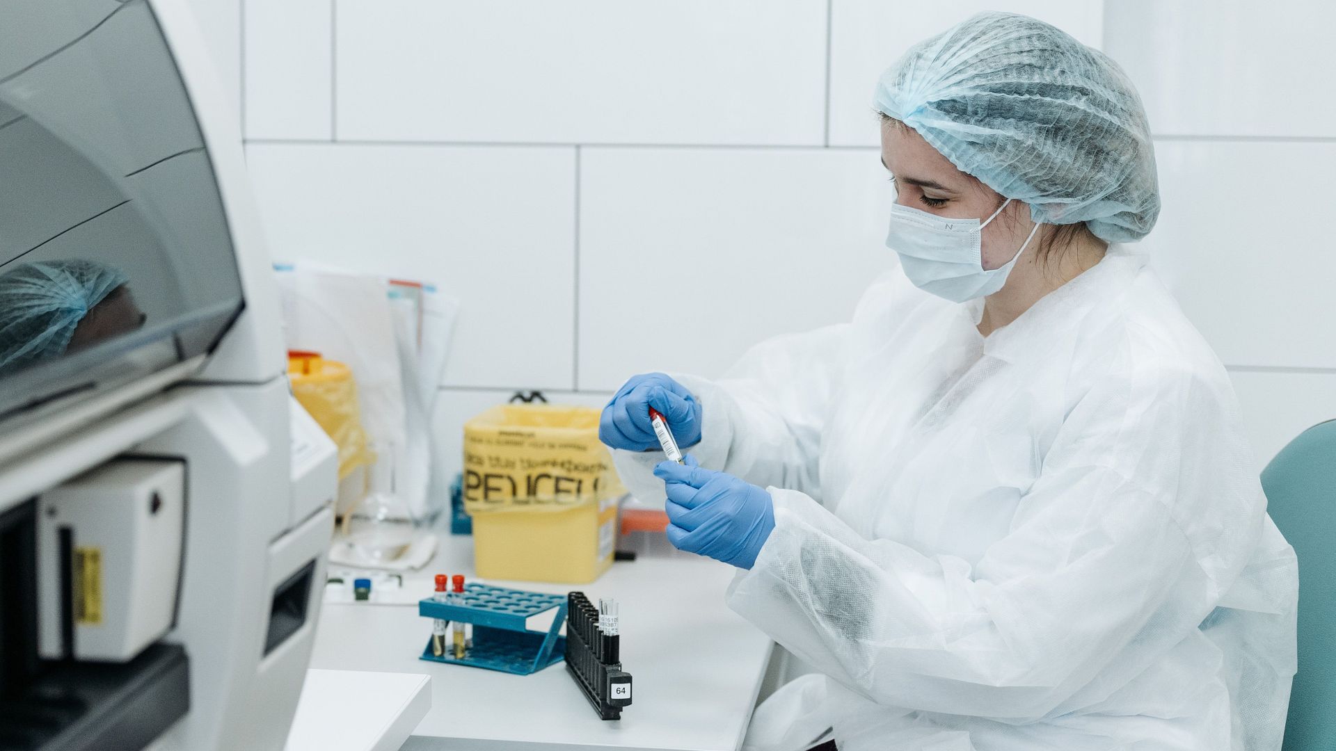 Scientist in protective gear examining samples in a medical lab setting, focusing on research.
