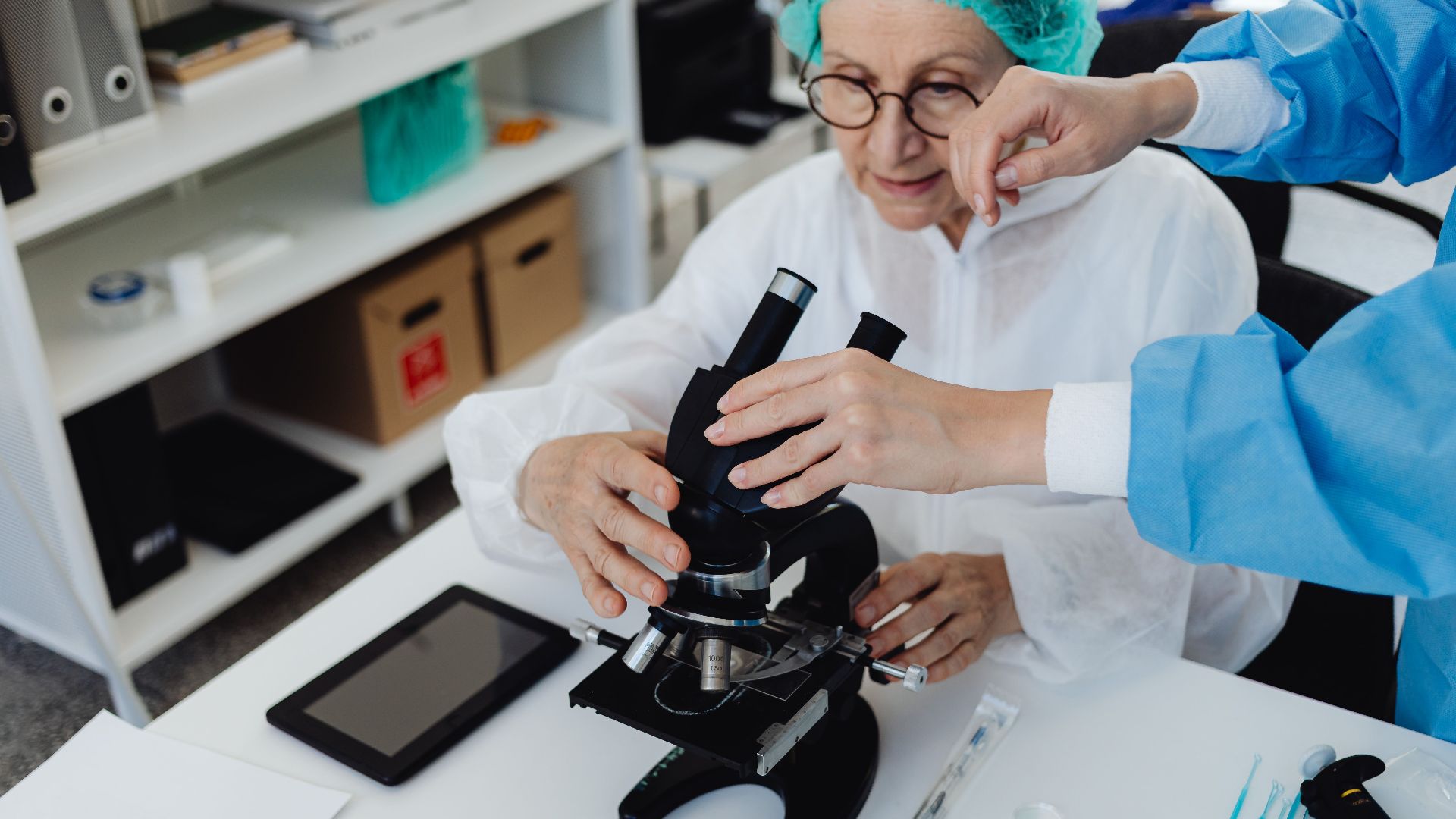 Senior scientist using a microscope with assistance in a laboratory setting, demonstrating research and analysis.