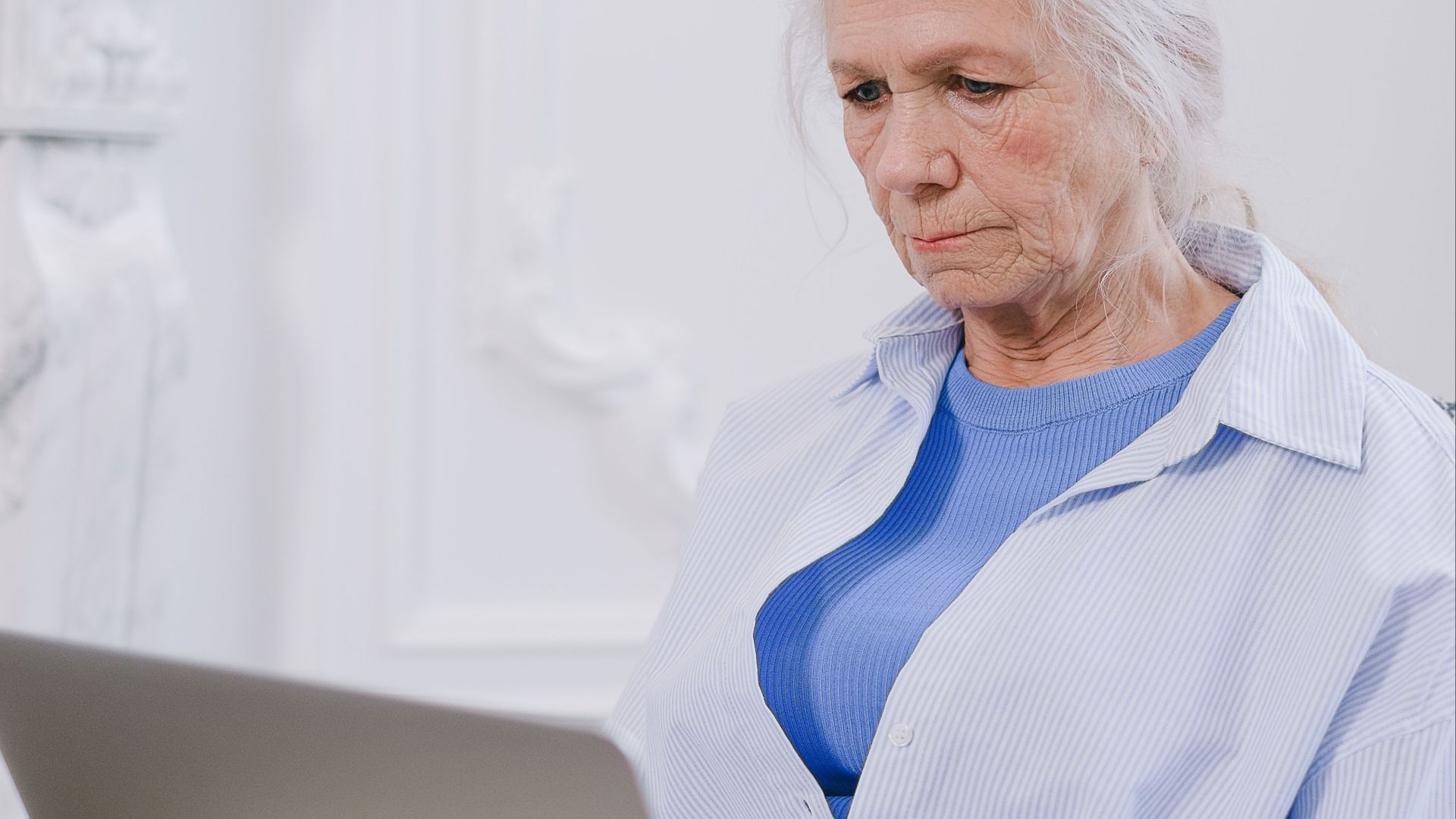 An elderly woman with white hair using a laptop indoors, showcasing technology use.