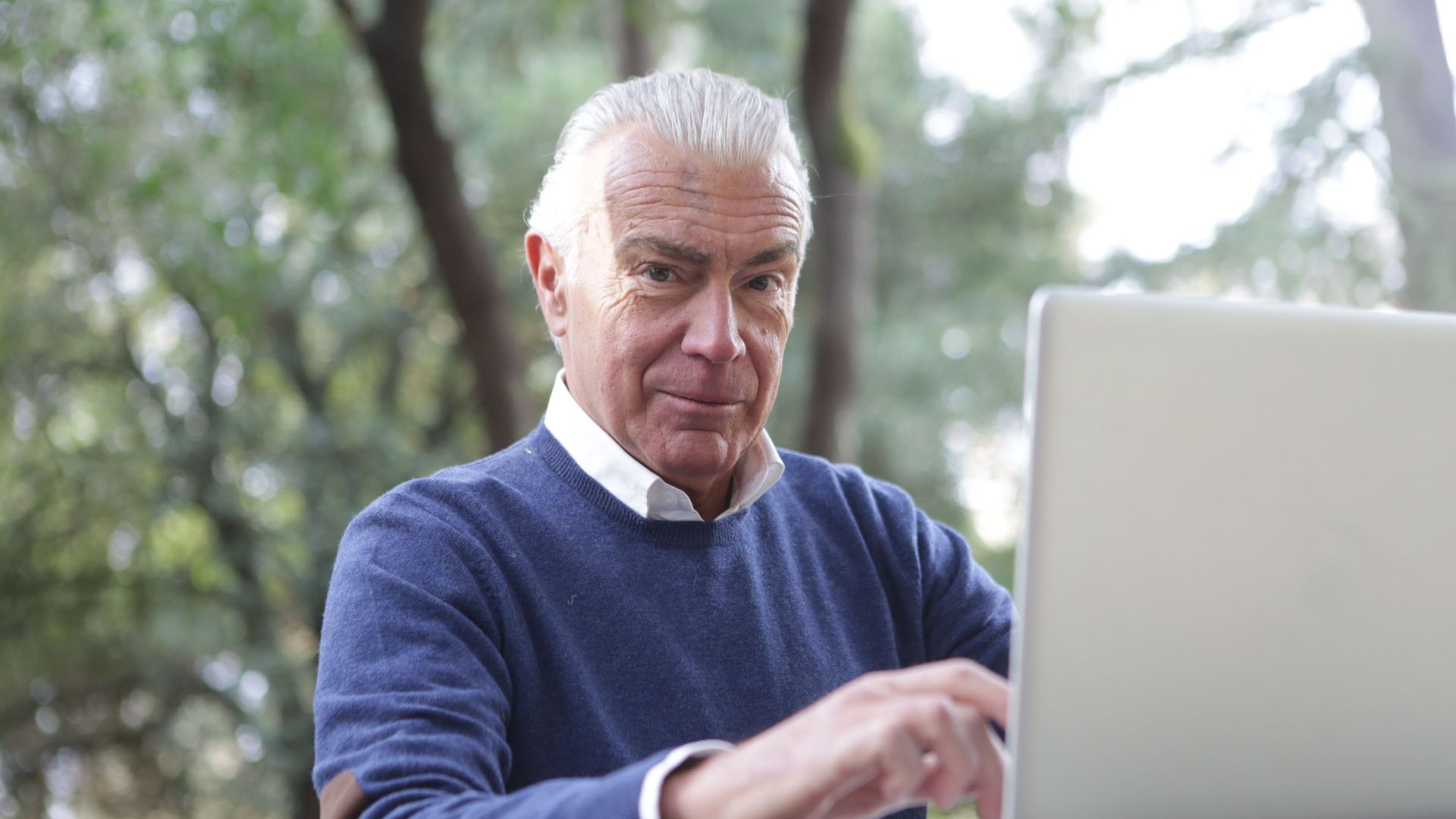 Senior man enjoying remote work on a laptop outdoors, embracing technology in nature.