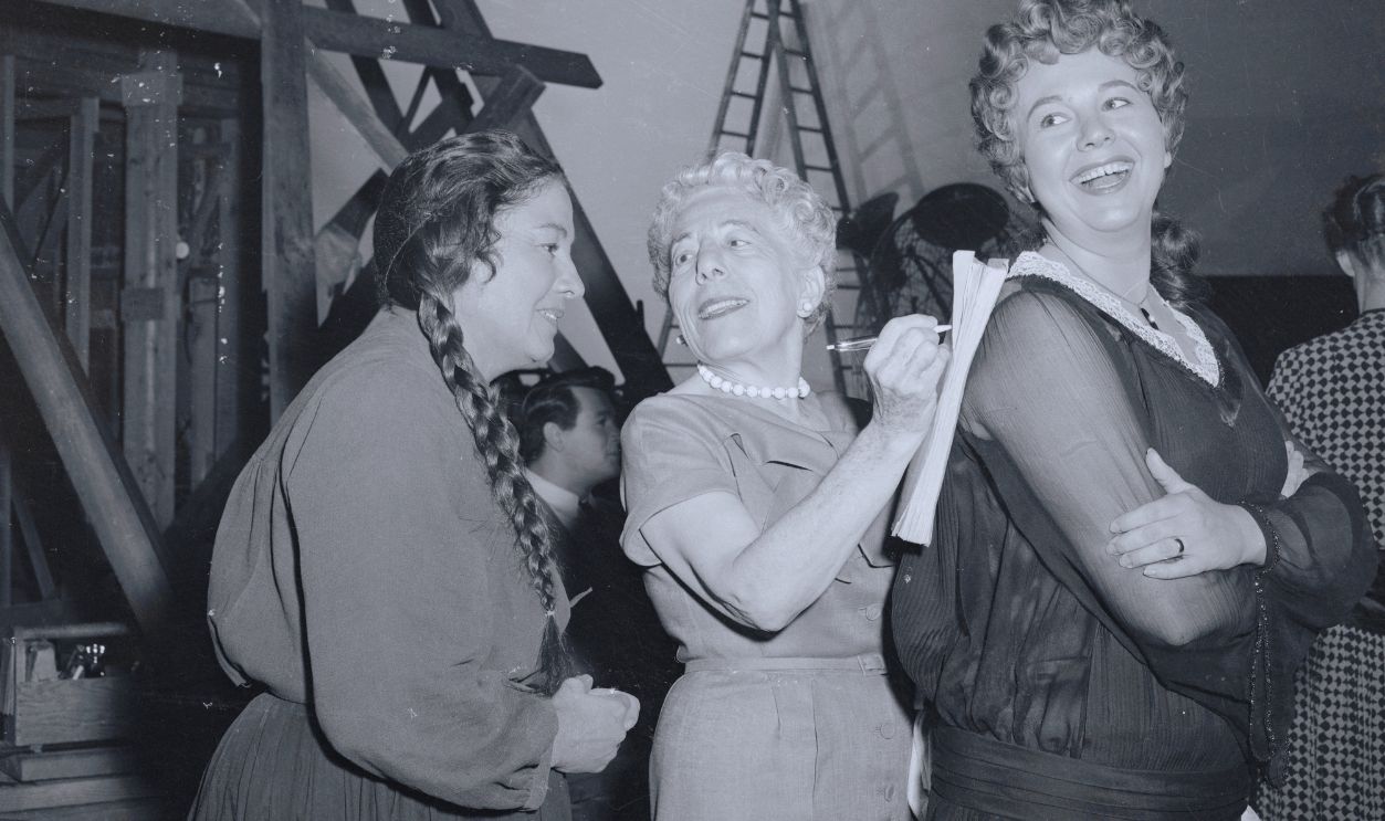 Gettyimages - 517757896, Author-Graph. It's usually the movie star who hands out the autograph, but this time it's the writer -- novelist Edna Ferber, (Center), uses Jane Withers' back to autograph a script of Giant, for Tina Menard, (Left). Miss Ferber wrote the book which is being made into a film. Former child star Miss Withers and actress Menard are made up for their roles in the picture. 