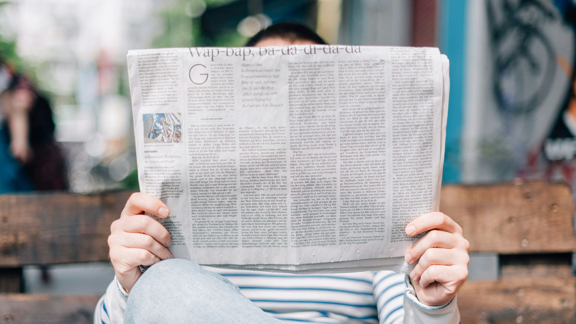 man sitting on bench reading newspaper