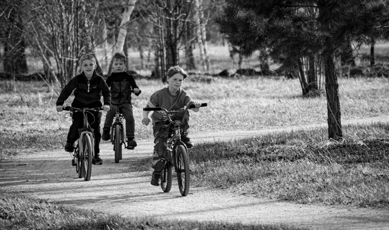Black and white photo of three kids cycling on a path through a park