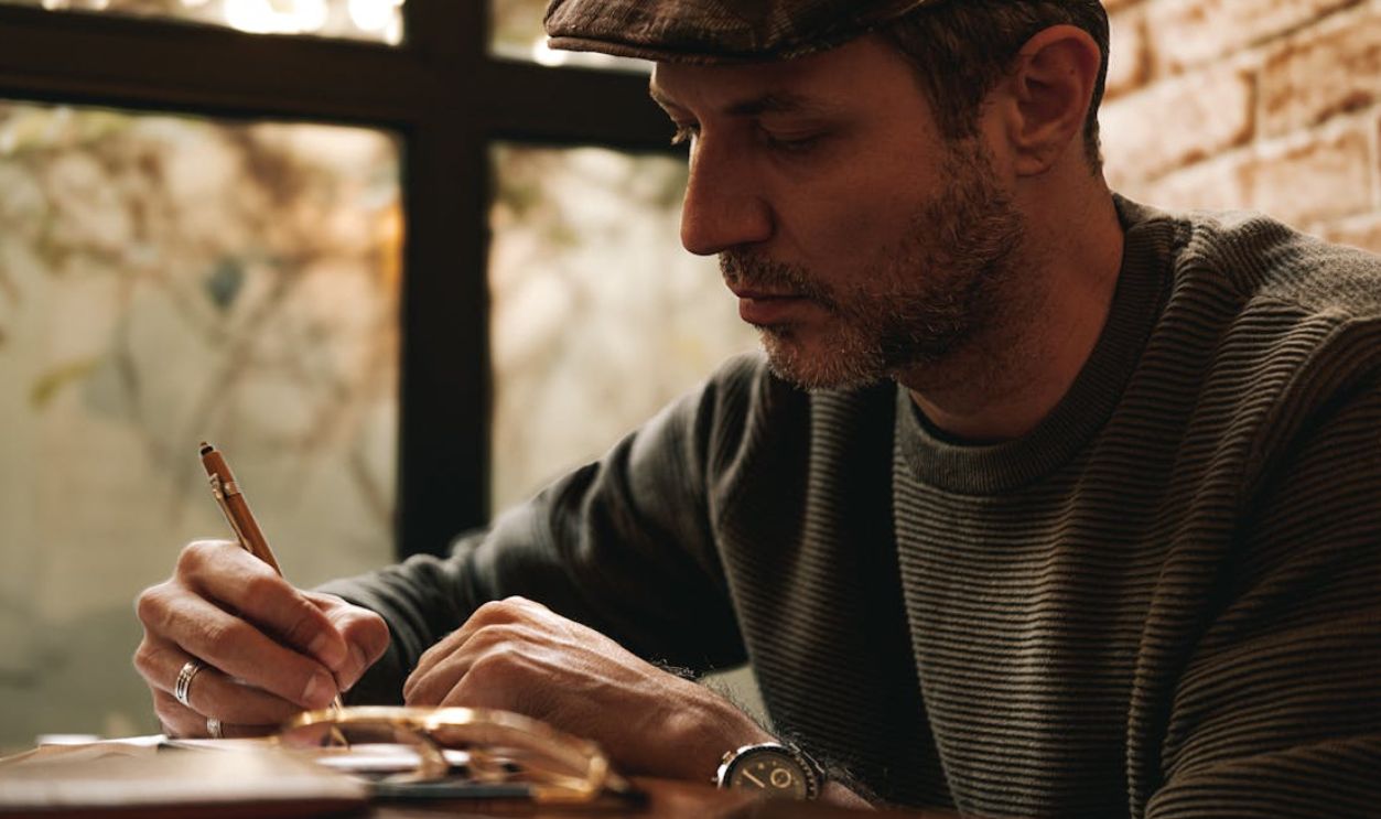 Thoughtful man writing in a notebook with a pen in a warm, cozy indoor environment