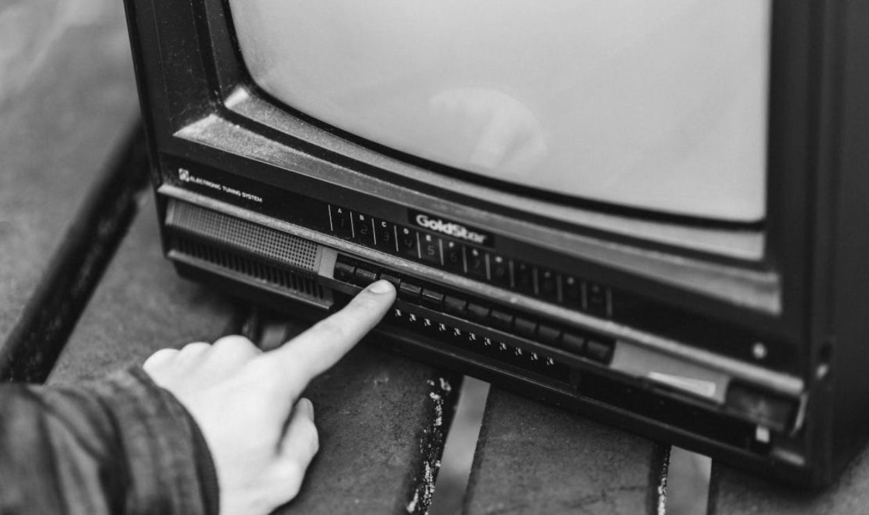 Black and white image of a hand pressing a button on a vintage TV set, evoking retro nostalgia