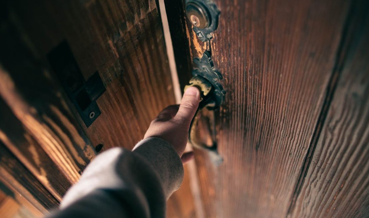 Close-up view of a hand opening a vintage wooden door with ornate handle, creating a warm and inviting atmosphere.