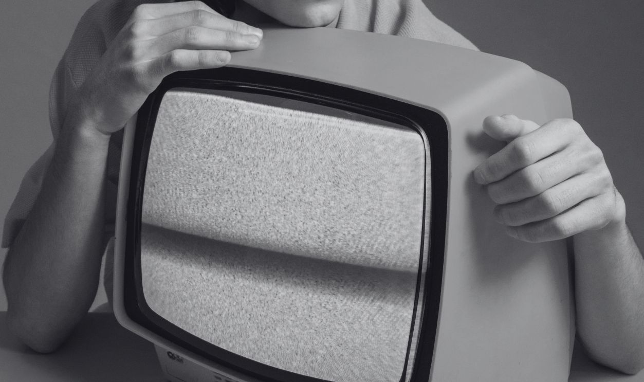 Stylish young man with curly hair poses with a vintage yellow TV in a retro setting