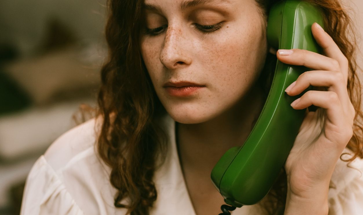 A pensive redhead woman uses a vintage green telephone, creating a nostalgic indoor scene