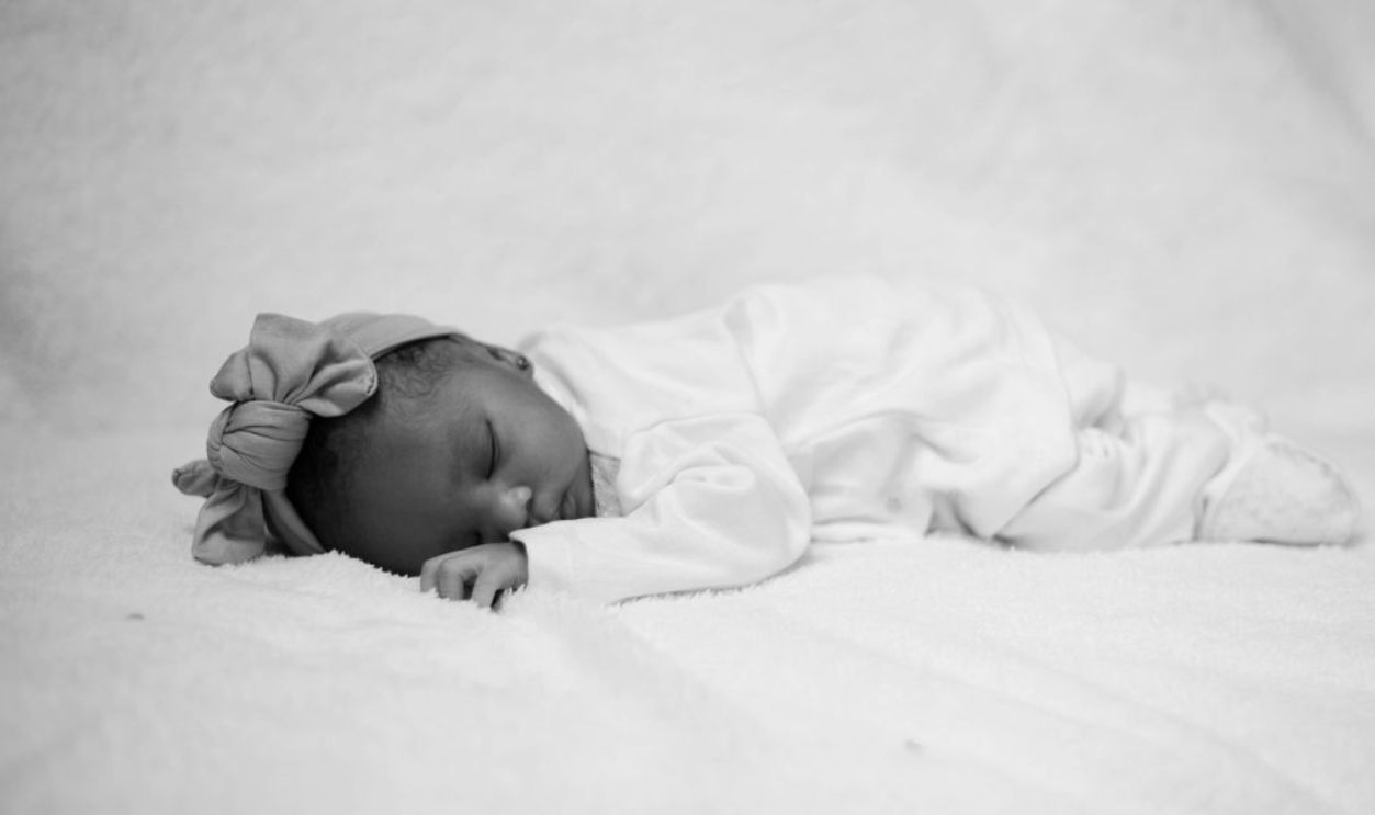 Black and white image of a newborn baby sleeping peacefully in a soft white setting