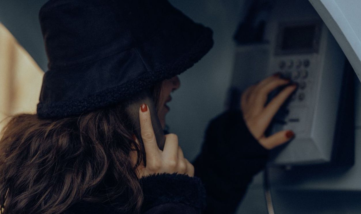 A woman in a retro hat makes a call from a public telephone in Fethiye, Turkiye, evoking nostalgia