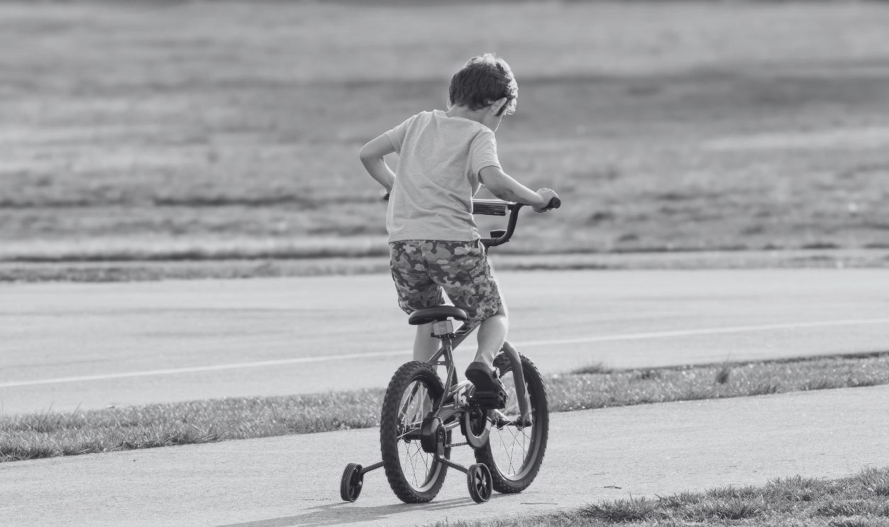 Young boy riding a bicycle with training wheels in a park on a sunny day