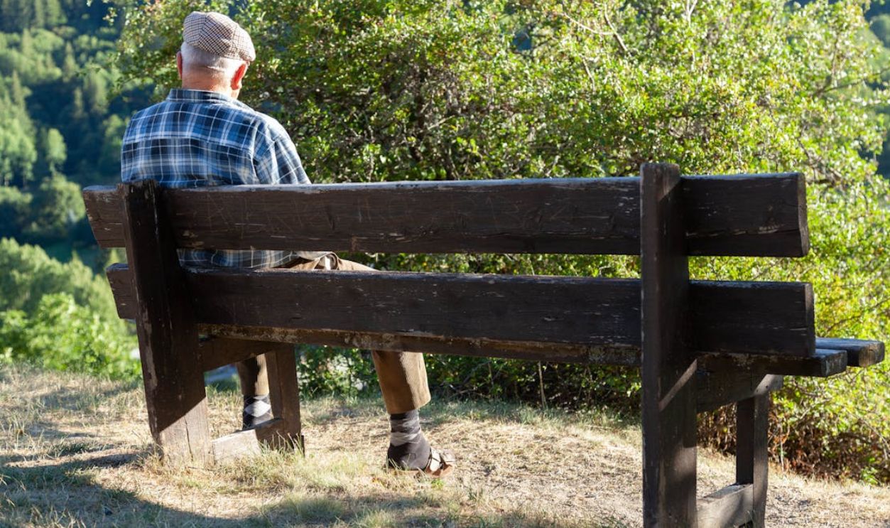 Elderly man in hat sitting on a bench in a peaceful rural setting in Briancon, France.