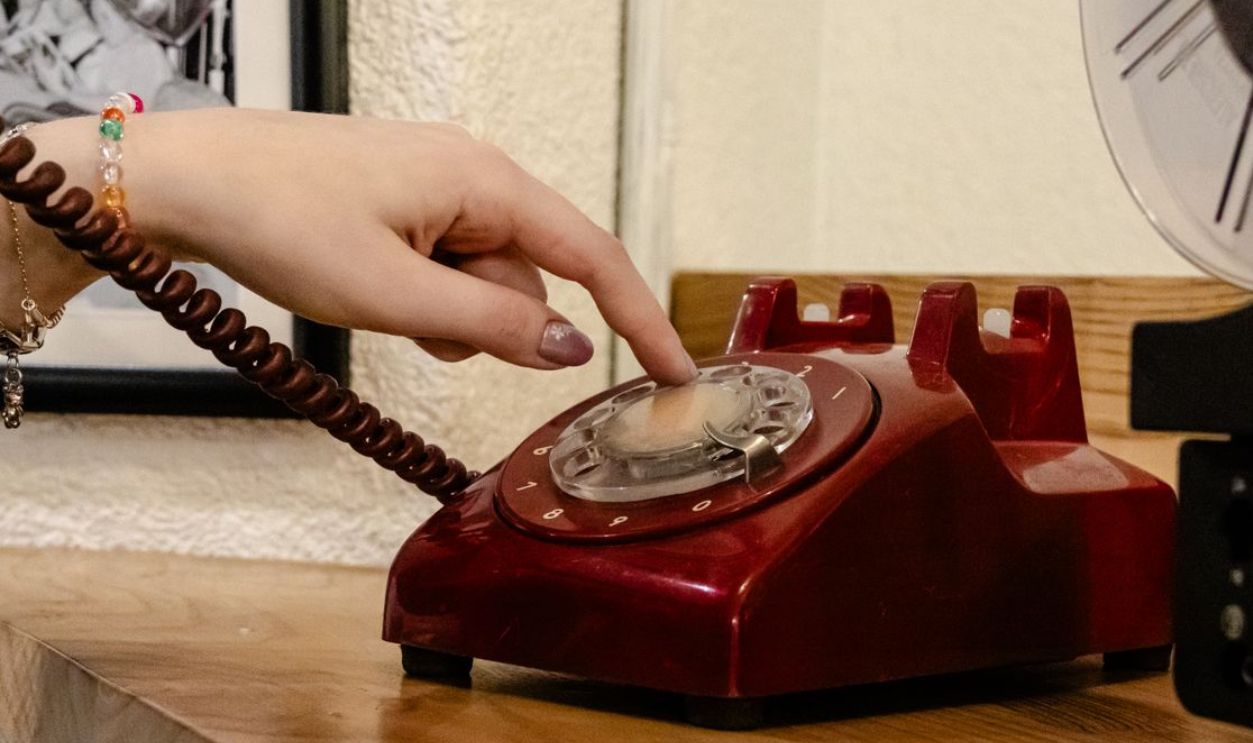 A close-up of a hand dialing a classic red rotary phone, capturing nostalgia